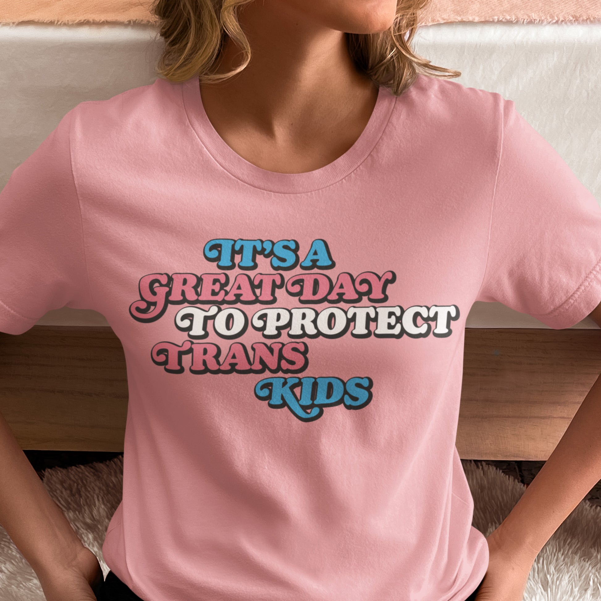 Model wearing trans rights T-shirt featuring pastel typography and the phrase “It’s A Great Day To Protect Trans Kids” supporting transgender youth.