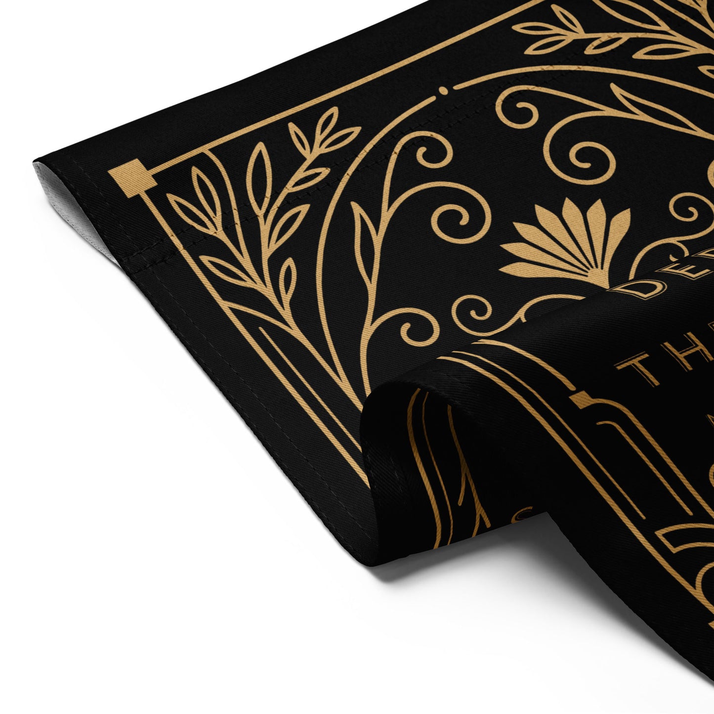 Folded black garden flag revealing repeated gold Art Deco patterns and portions of the “Keep The Immigrants” protest text, highlighting fabric texture and print clarity.