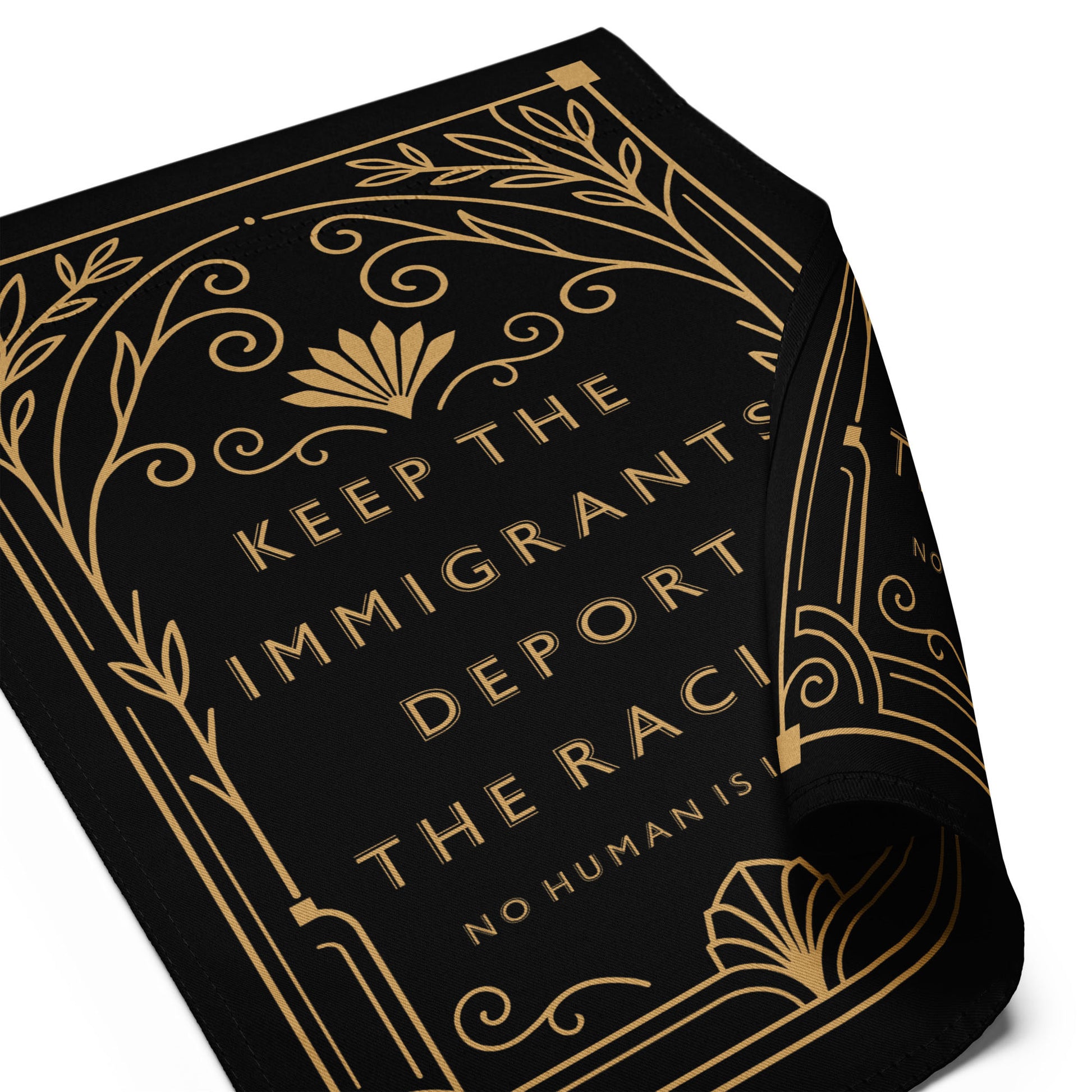 Close-up of black garden flag fabric showing gold Art Deco linework, ornamental corner flourishes, and crisp serif lettering from the “Keep The Immigrants” design by Blue Wave USA.