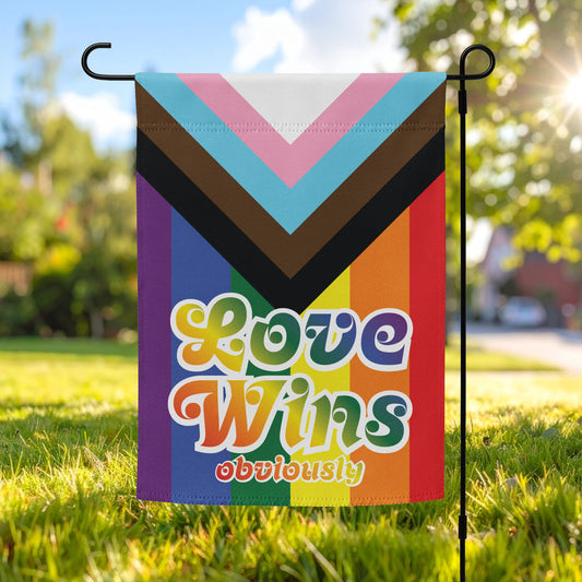 Progress pride garden flag displayed outdoors on a metal stand, featuring chevron pride stripes and bold retro lettering reading “LOVE WINS obviously.”