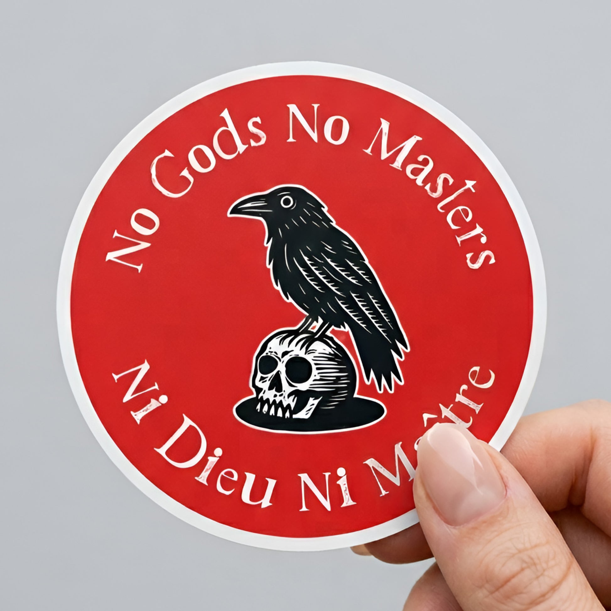 Round sticker featuring a black raven perched on a skull over red background with “No Gods No Masters / Ni Dieu Ni Maître” text, anti-authoritarian activist design.