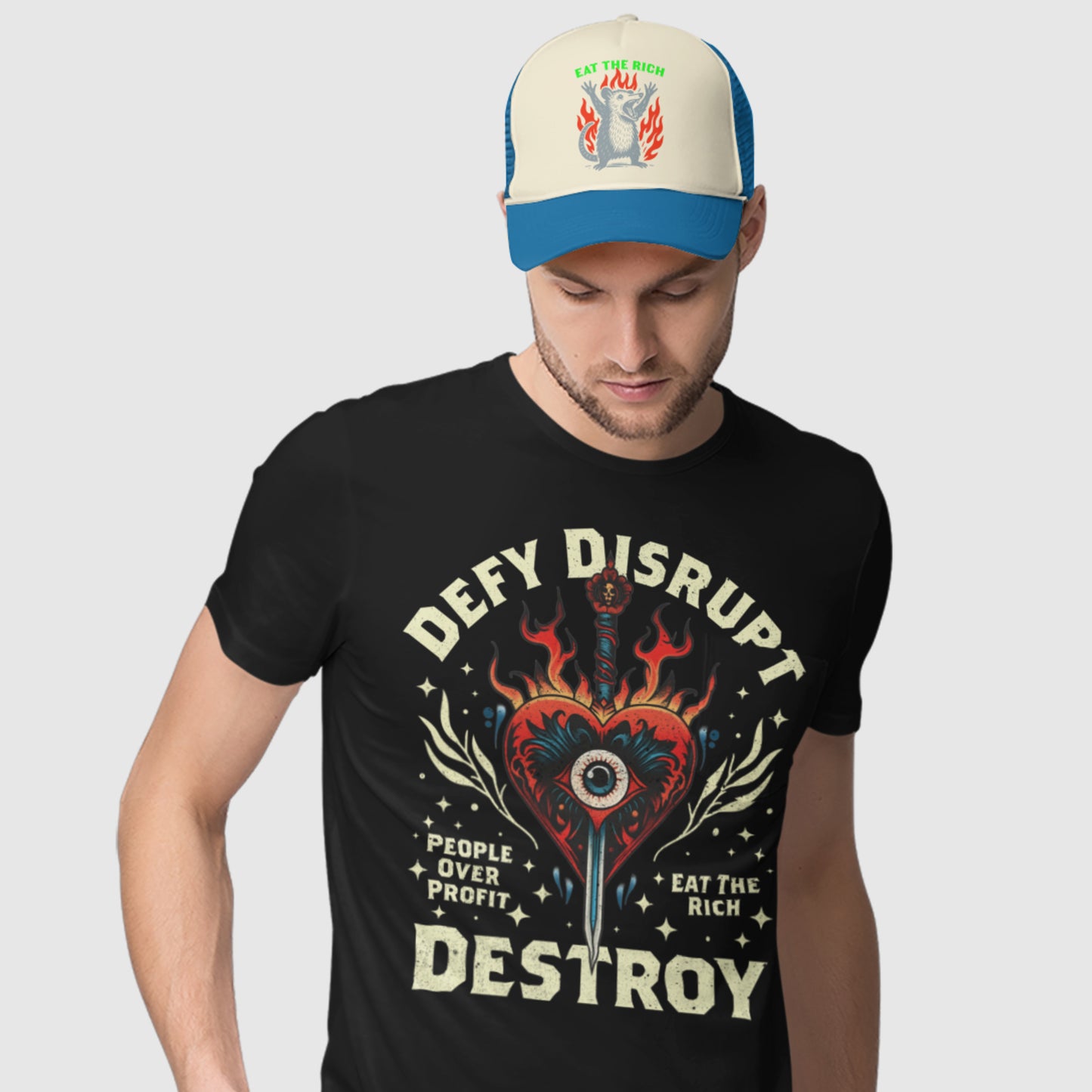 Model wearing black unisex t-shirt featuring flaming heart and eye illustration with protest phrases “Defy Disrupt Destroy,” “People Over Profit,” and “Eat The Rich.”