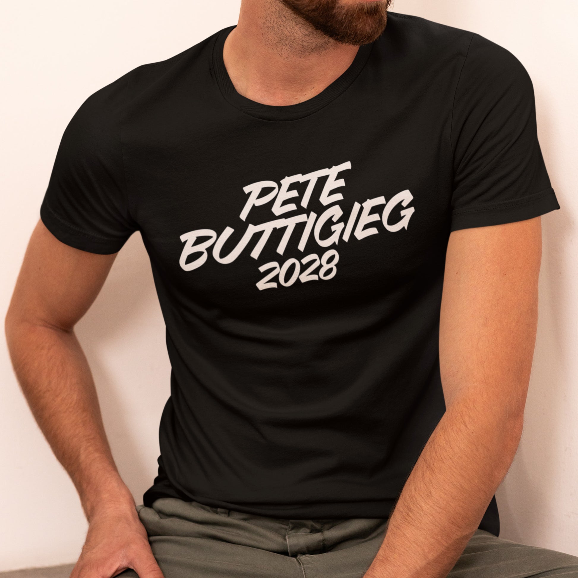 Model wearing black unisex classic tee featuring bold white script text reading “PETE BUTTIGIEG 2028.”
