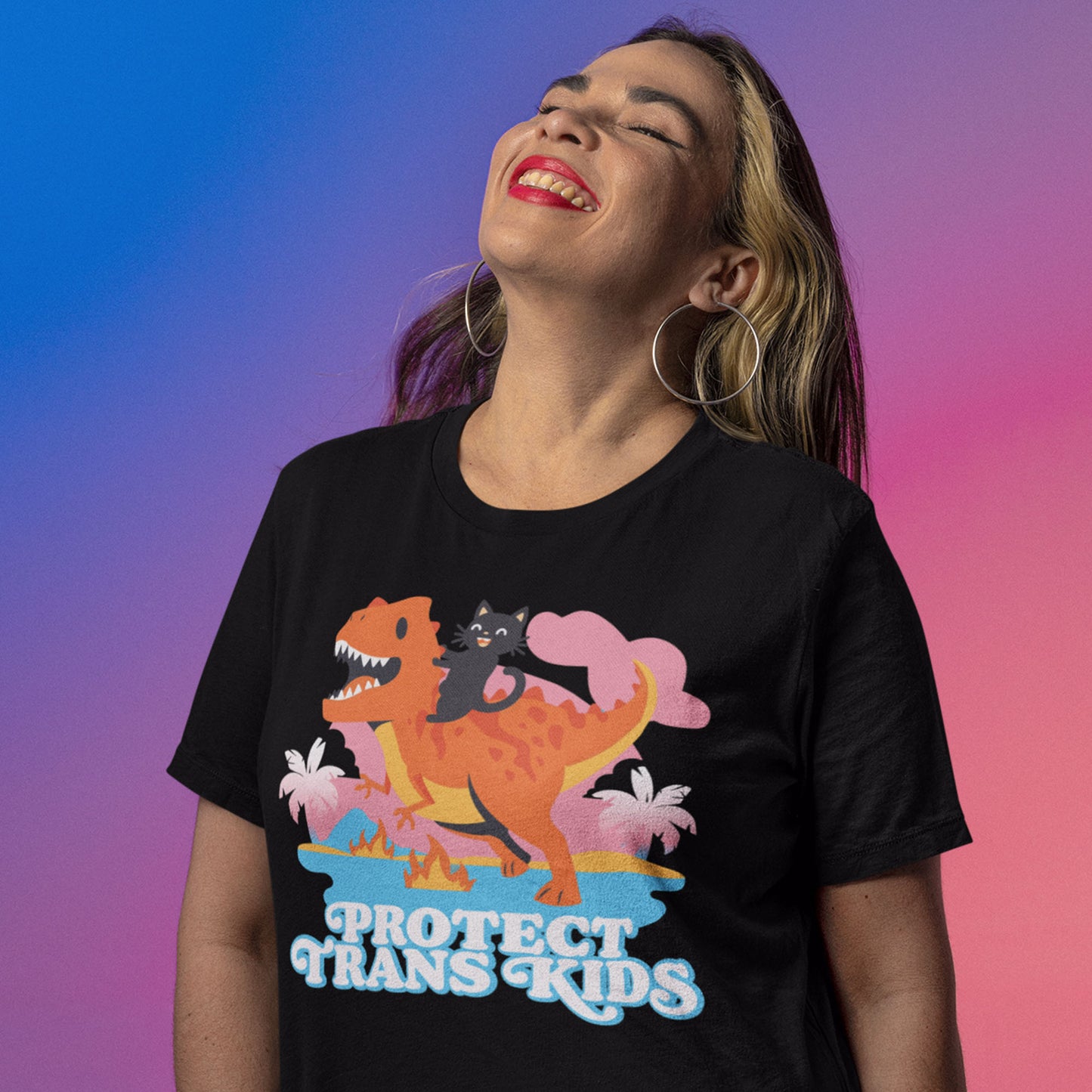 Model wearing black unisex t-shirt with vibrant cartoon dinosaur and ally cat graphic above retro blue typography reading “Protect Trans Kids.”
