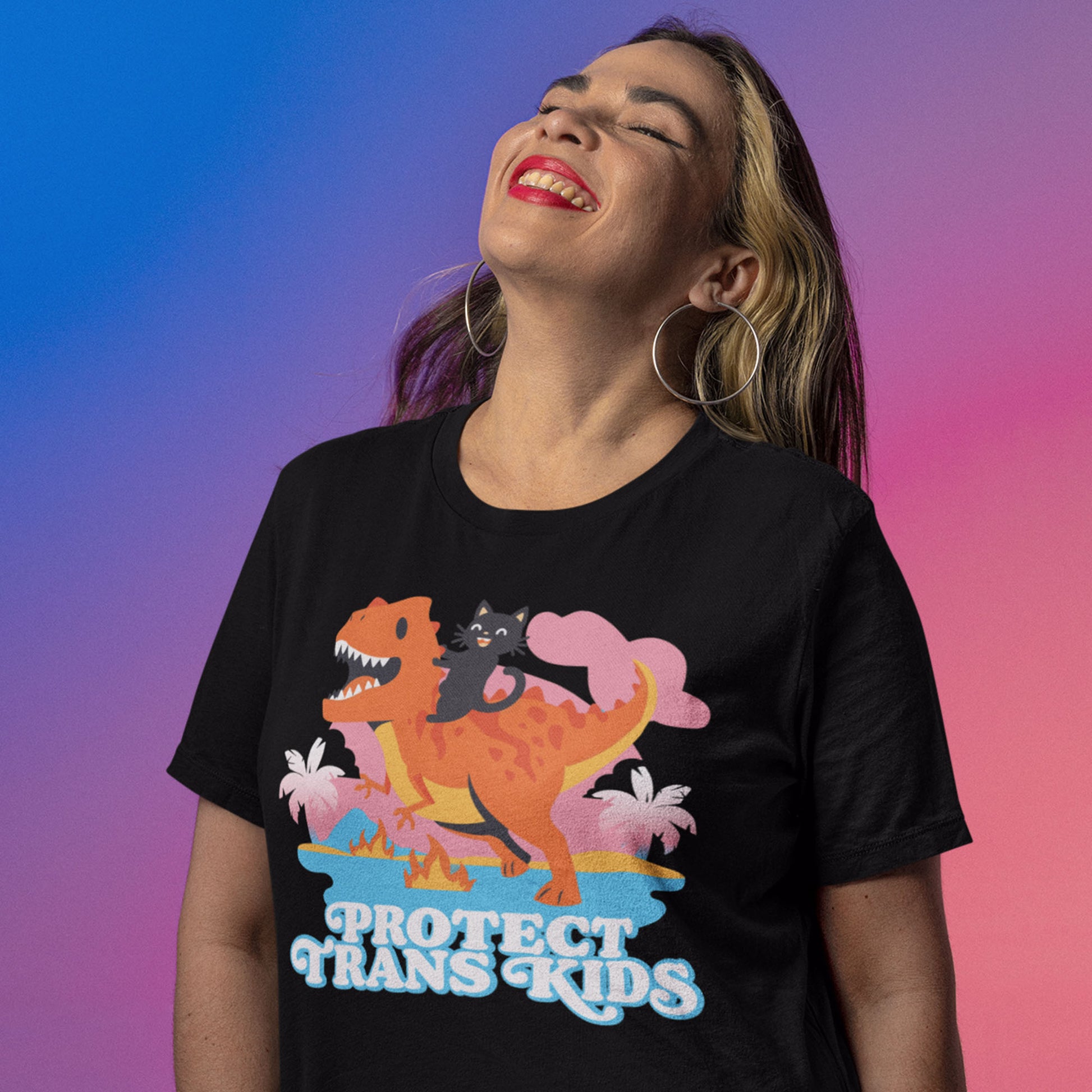 Model wearing black unisex t-shirt with vibrant cartoon dinosaur and ally cat graphic above retro blue typography reading “Protect Trans Kids.”