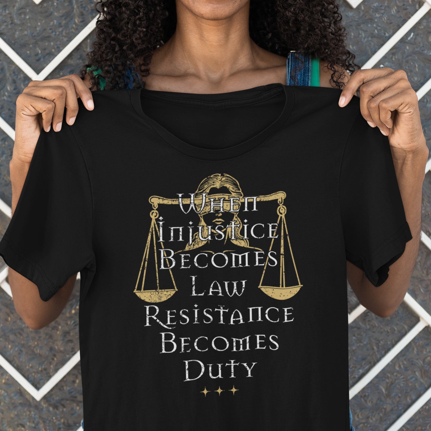 Model holding black unisex t-shirt featuring Lady Justice scales illustration with gold and white serif typography, centered progressive justice graphic from Blue Wave USA.