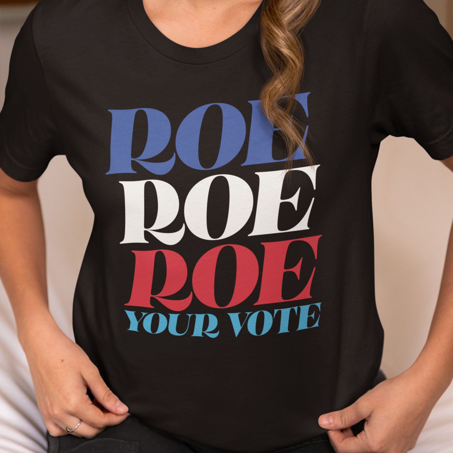 Model wearing black unisex t-shirt featuring bold stacked typography reading “Roe Roe Roe Your Vote” in patriotic red, white, and blue colors.