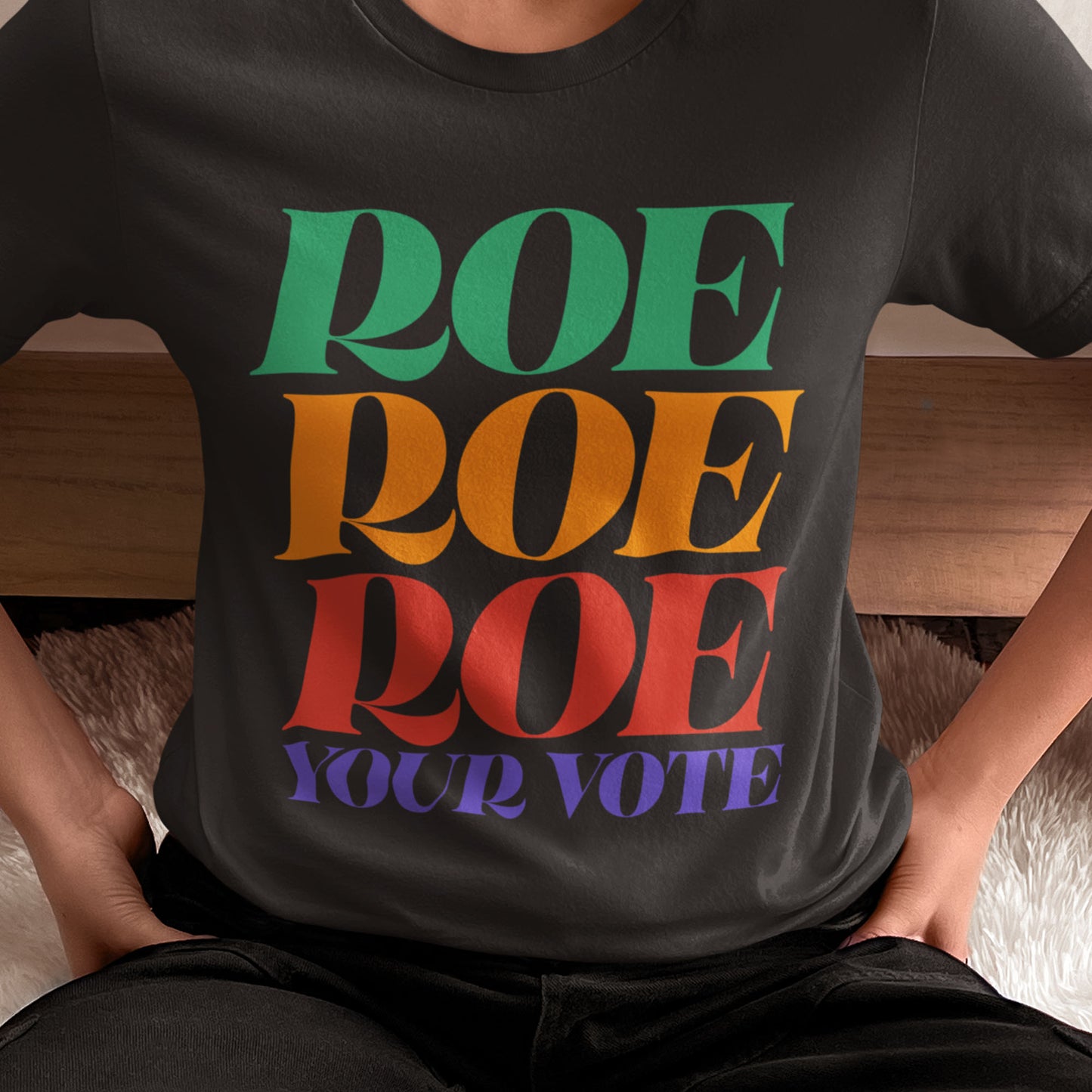 Model wearing black unisex t-shirt featuring bold stacked rainbow typography reading “Roe Roe Roe Your Vote.”