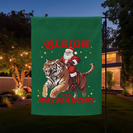 “Sleigh the Patriarchy” Christmas garden flag featuring Santa riding a tiger with festive stars, displayed outdoors at night.