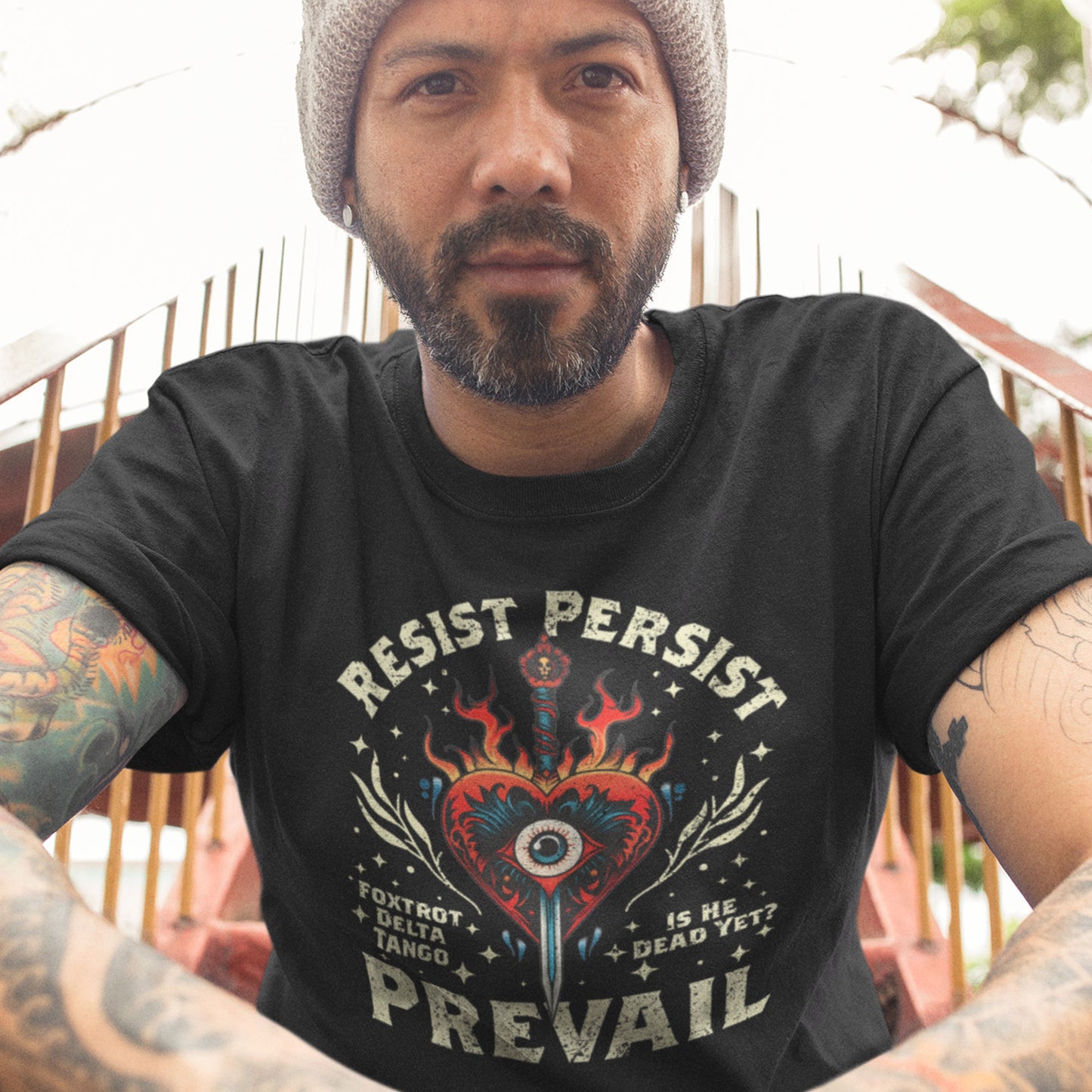 Model wearing black unisex t-shirt featuring flaming heart dagger illustration and distressed text “RESIST PERSIST PREVAIL,” with small phrases “FOXTROT DELTA TANGO” and “IS HE DEAD YET?”