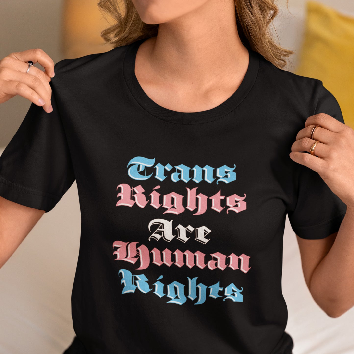 Model wearing black unisex t-shirt featuring gothic stacked typography reading “Trans Rights Are Human Rights” in trans pride colors.