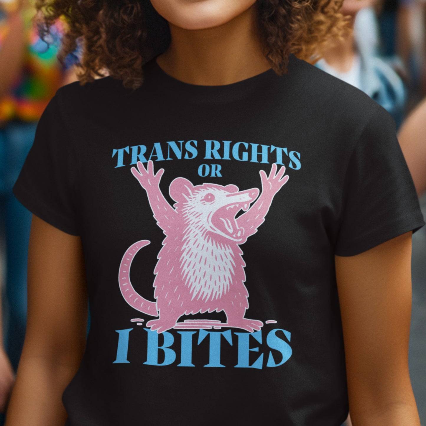 Model wearing the “Trans Rights or I Bites” black t-shirt by Blue Wave USA, showing a pink opossum with raised paws and bold blue lettering.