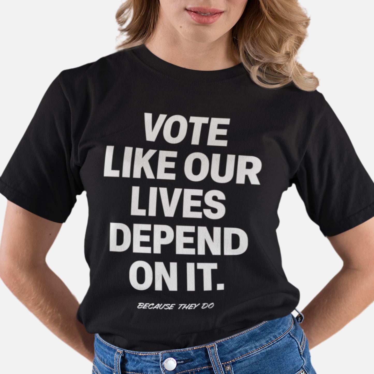 Person wearing the black Vote Like Our Lives Depend On It shirt, paired with jeans. The minimalist typography and serious tone amplify the message — a core campaign piece from Blue Wave USA.