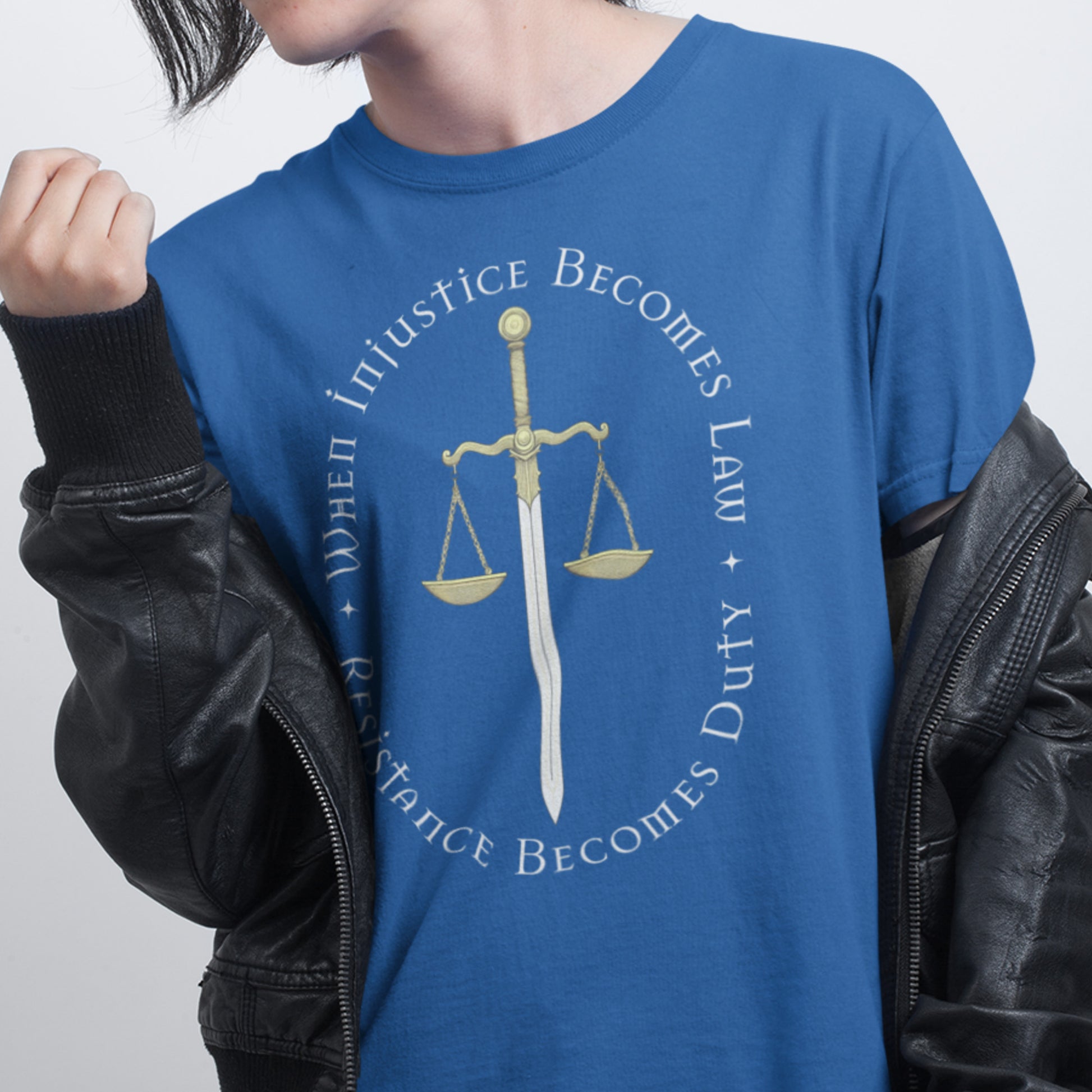 Person wearing the “When Injustice Becomes Law” blue t-shirt layered under a leather jacket, showing the bold gold justice scale and activist quote.