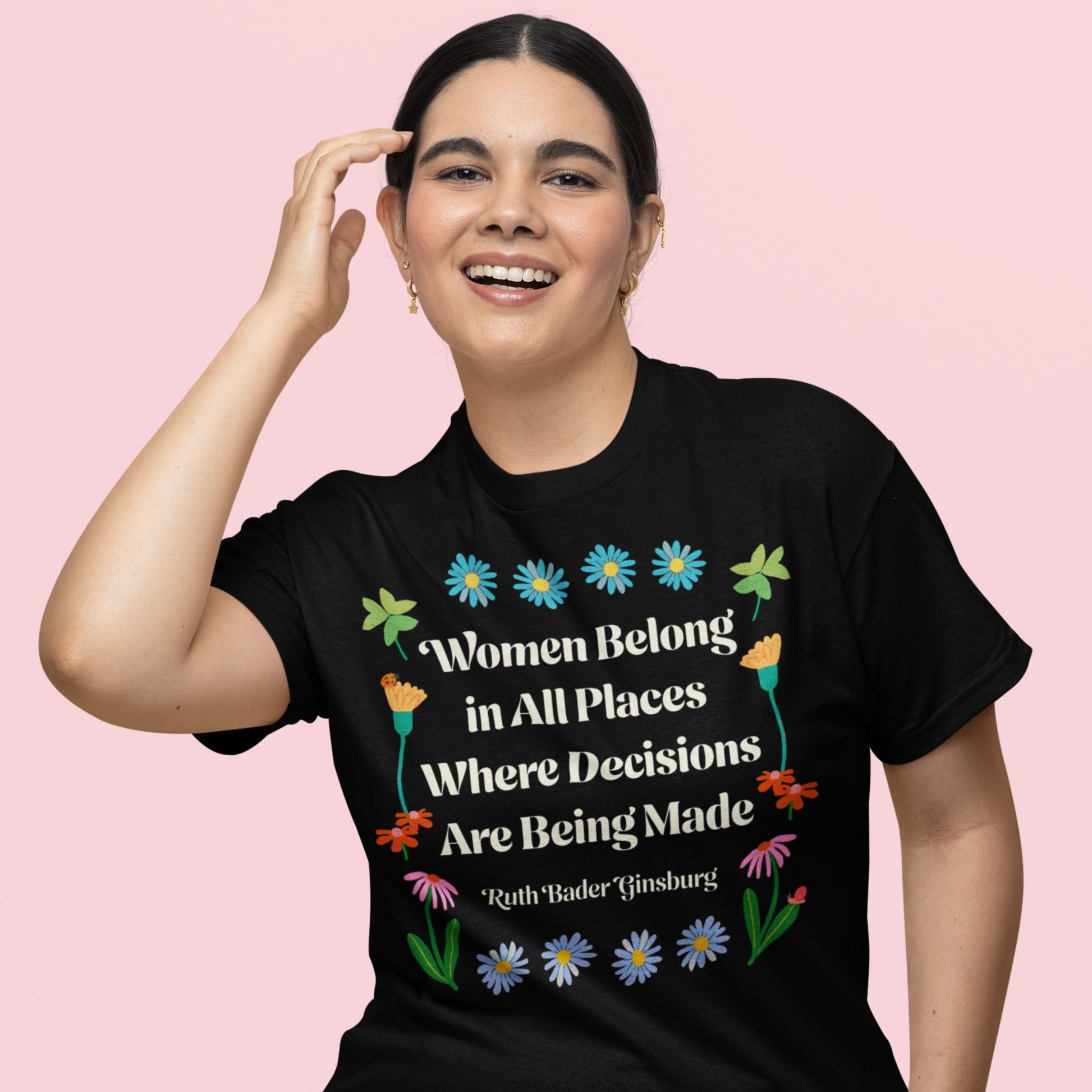 Model wearing black unisex t-shirt with floral folk-art design surrounding Ruth Bader Ginsburg quote reading “Women Belong In All Places Where Decisions Are Being Made.”