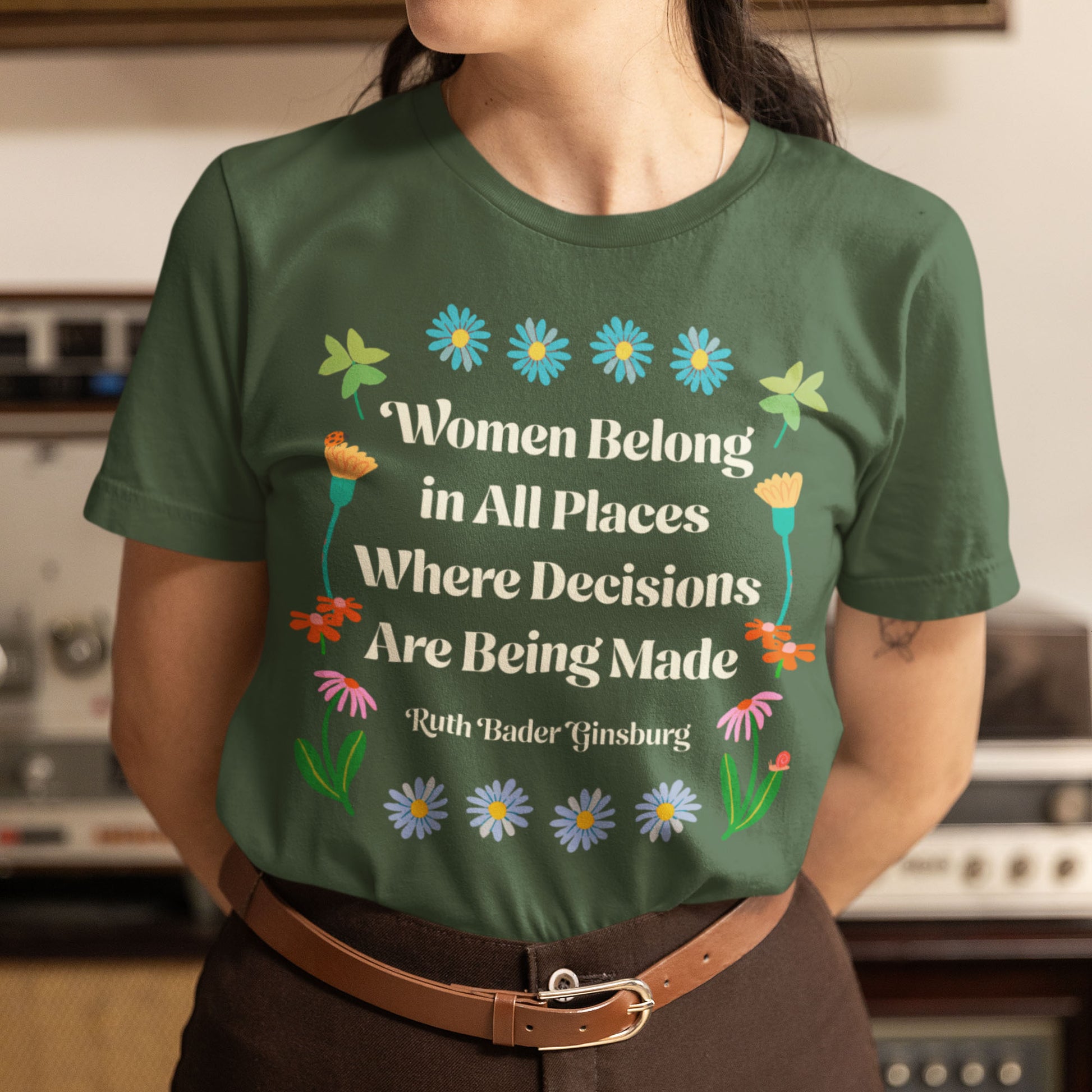 Model wearing green unisex t-shirt featuring floral illustration and typography reading “Women Belong in All Places Where Decisions Are Being Made – Ruth Bader Ginsburg,” progressive apparel from Blue Wave USA.