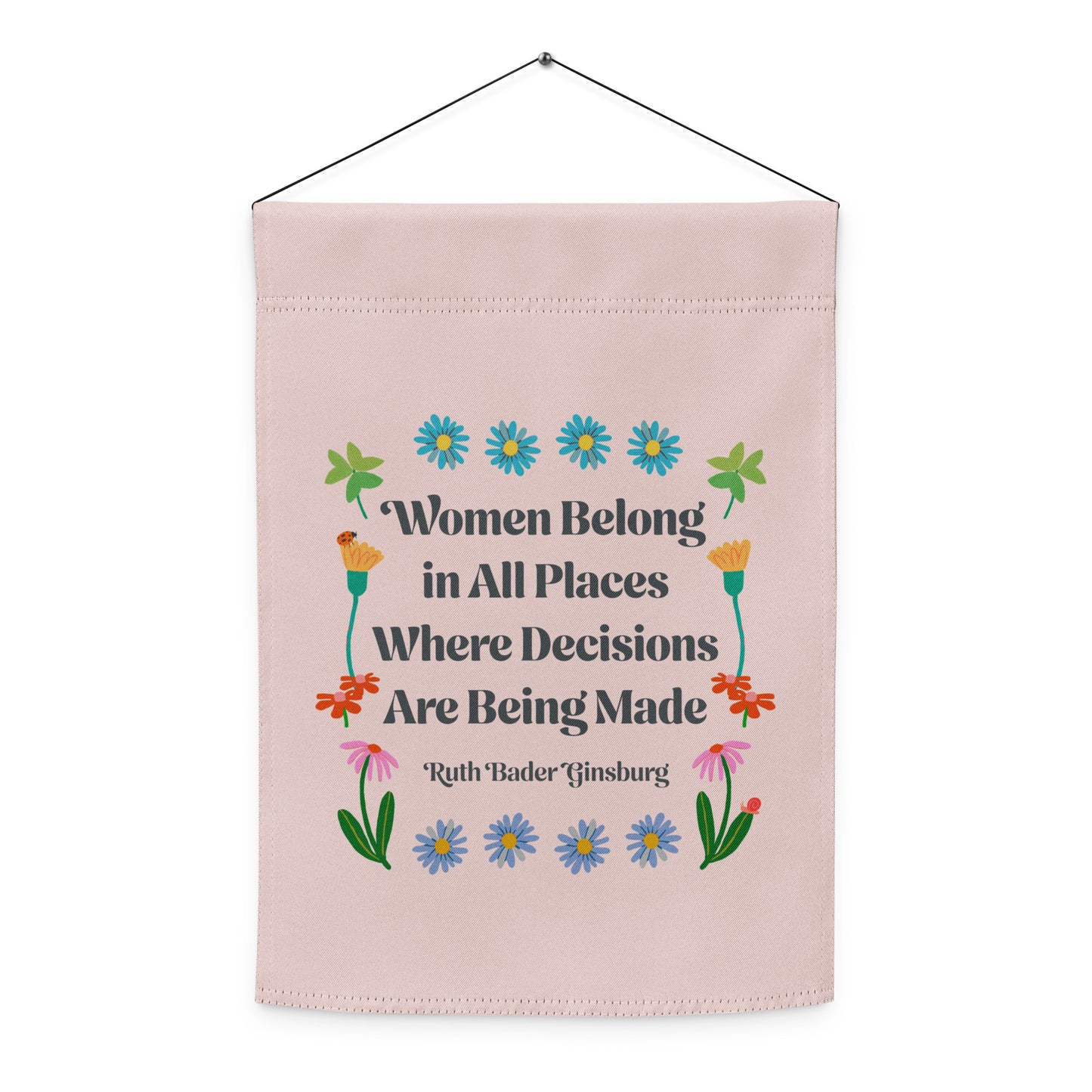 Indoor hanging view of the light pink garden flag, showcasing the full floral folk-art layout and the RBG quote “Women Belong in All Places Where Decisions Are Being Made,” by Blue Wave USA.