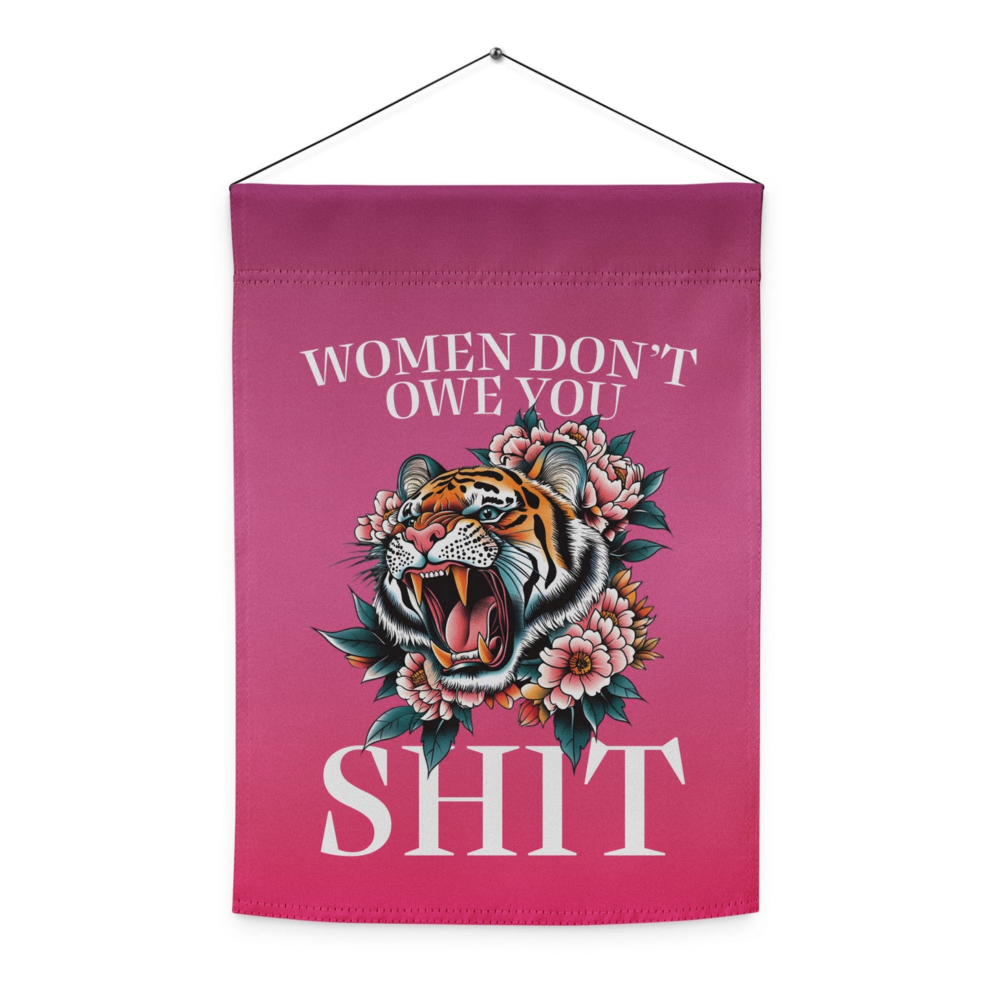Indoor hanging view of the garden flag, showing the full tiger illustration with floral framing and bold serif text reading “WOMEN DON’T OWE YOU SH*T,” from Blue Wave USA.