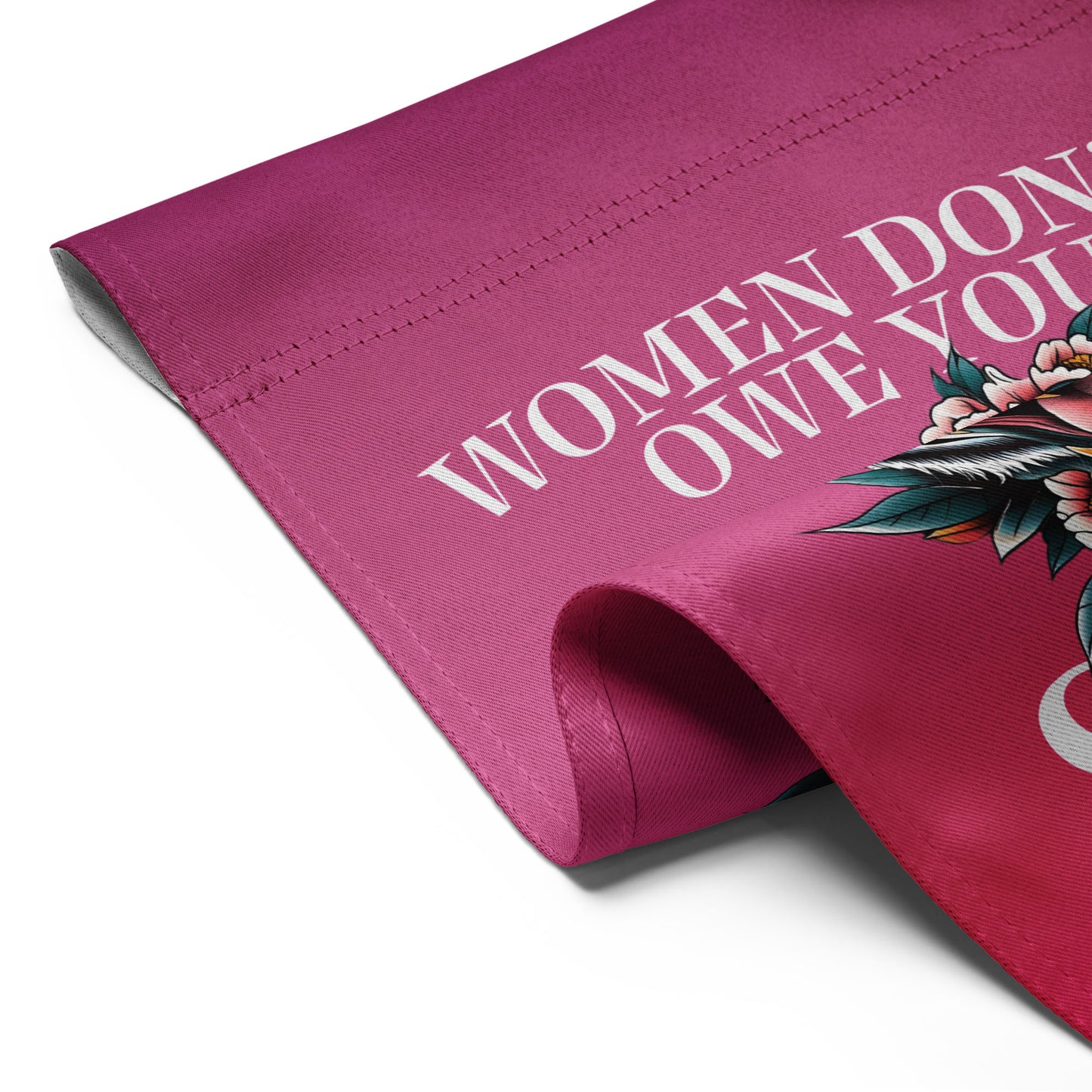 Close-up of the garden flag fabric edge, showing clean stitching, rich pink color, and partial typography from the phrase “WOMEN DON’T OWE YOU SH*T.”