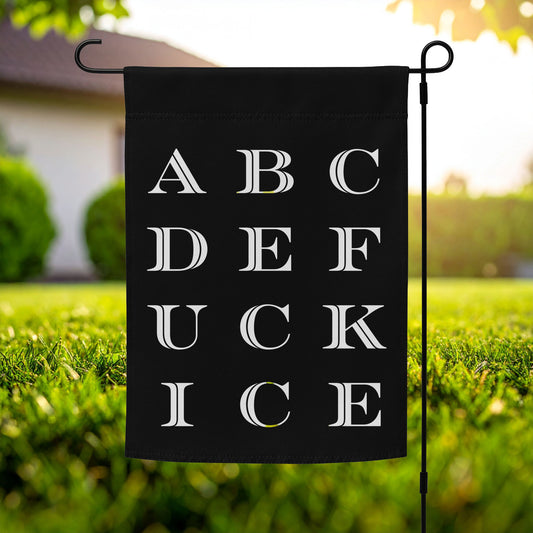 Garden flag featuring alphabet-style typography arranged in grid layout, white serif letters on black background, vertical design, printed message “ABCDEFUCKICE,” outdoor lawn display.