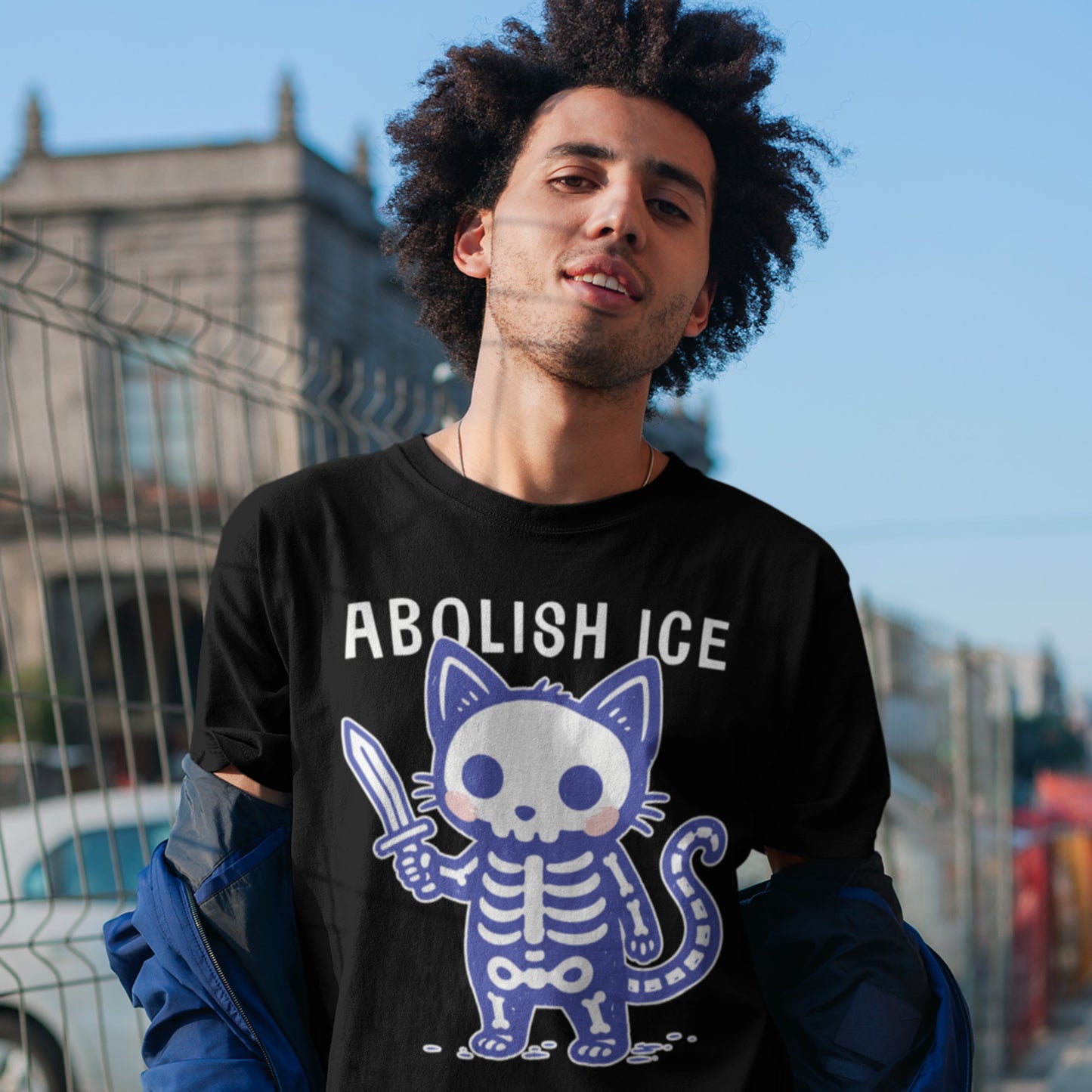 Person wearing the Abolish ICE Cute Skeleton Cat Unisex T-Shirt outdoors, featuring a playful skeleton cat holding a sword beneath bold “Abolish ICE” lettering for a striking immigration justice statement.