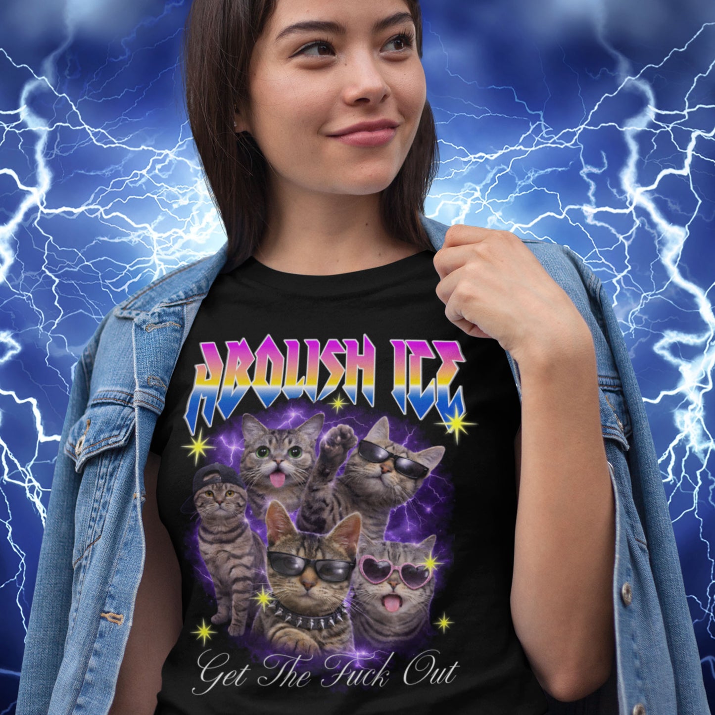 Model wearing black unisex t-shirt with illustrated cats, purple lightning background, rainbow “ABOLISH ICE” text, and cursive phrase “Get The Fuck Out,” casual street styling.