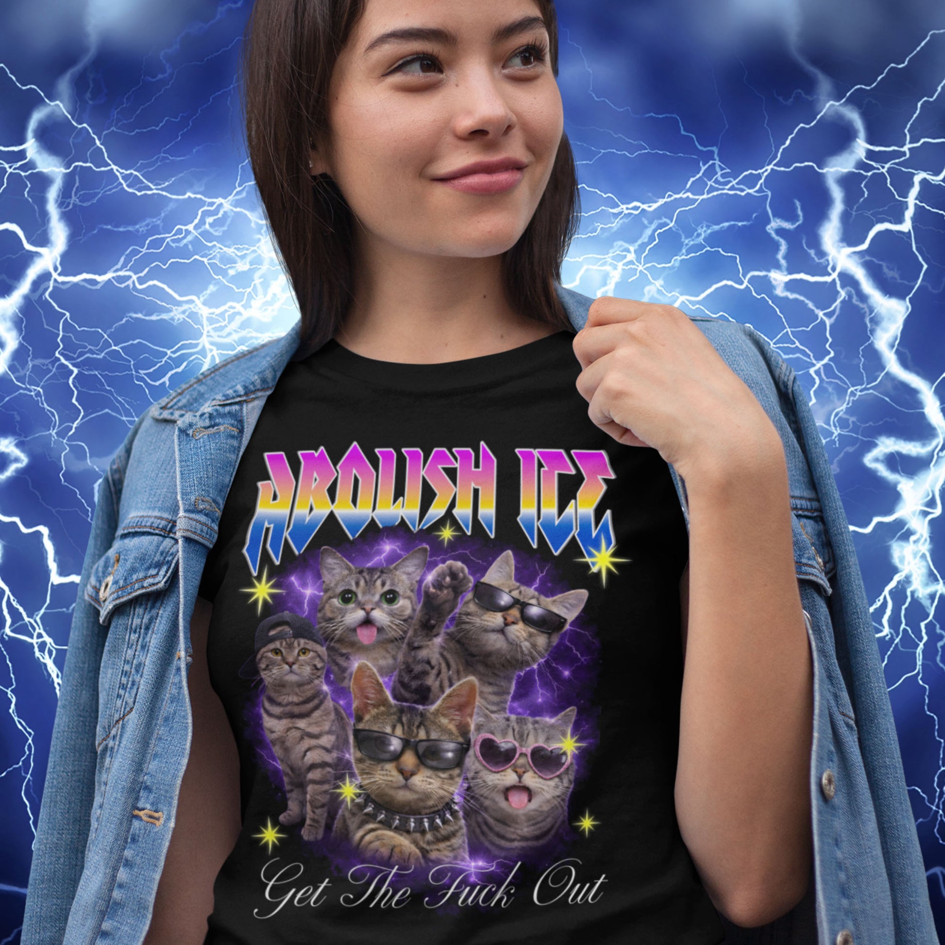 Model wearing black unisex t-shirt with illustrated cats, purple lightning background, rainbow “ABOLISH ICE” text, and cursive phrase “Get The Fuck Out,” casual street styling.