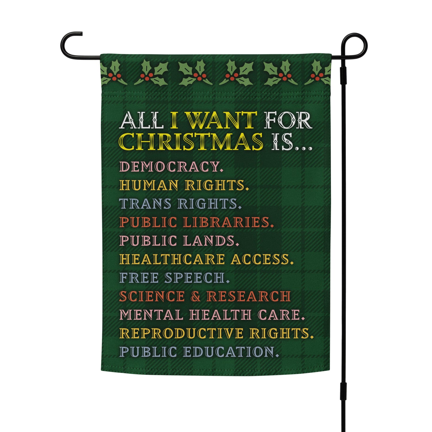 Green plaid garden flag on a metal stand featuring holly motifs and the printed message “ALL I WANT FOR CHRISTMAS IS…” followed by items such as human rights and free speech, designed by Blue Wave USA.