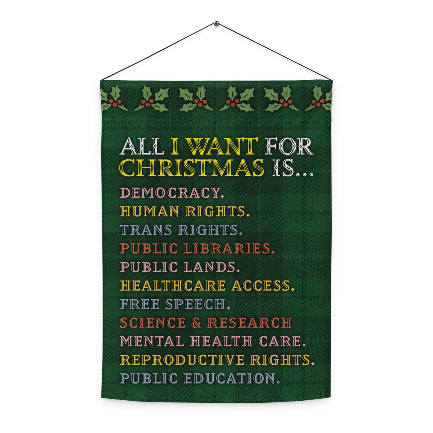 Green hanging garden flag with a plaid pattern and holly border, printed with the full “ALL I WANT FOR CHRISTMAS IS…” list including democracy, trans rights, healthcare access, and public education.