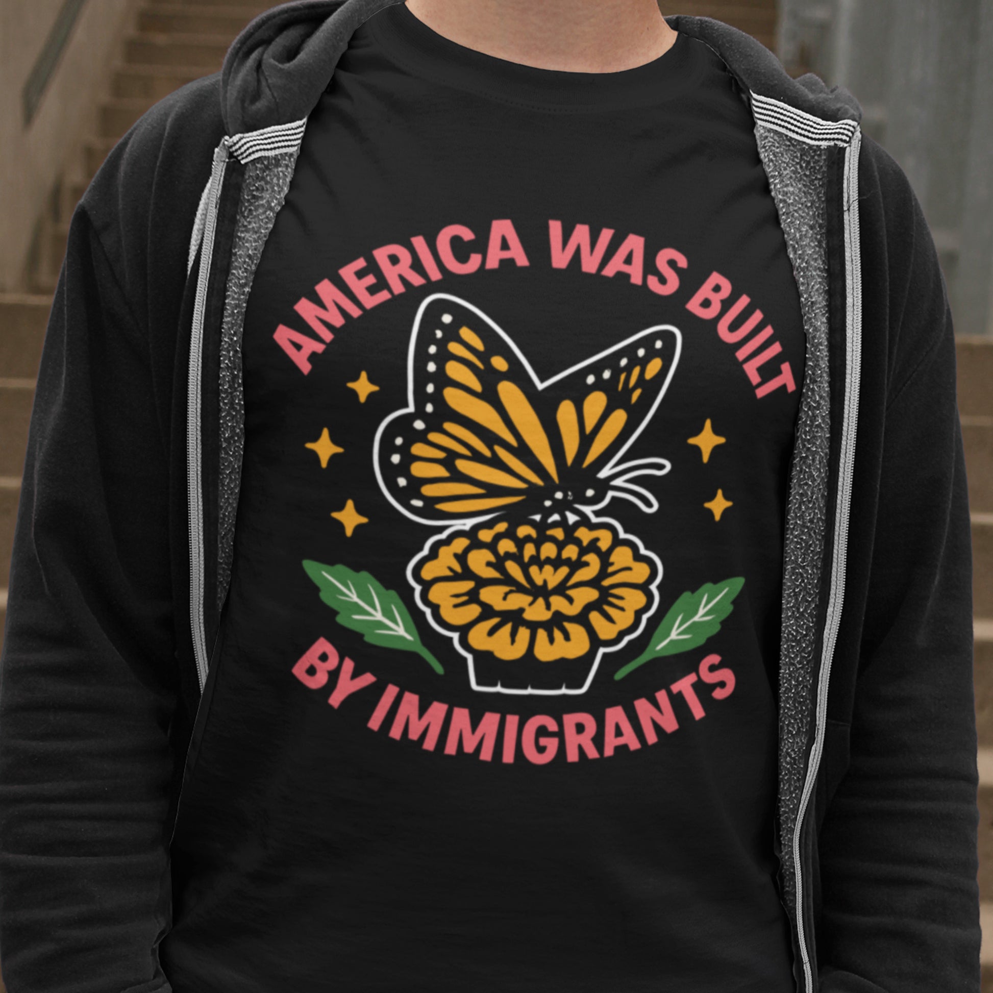 Person wearing “America Was Built by Immigrants” monarch butterfly shirt, Blue Wave USA progressive apparel promoting immigrant rights.