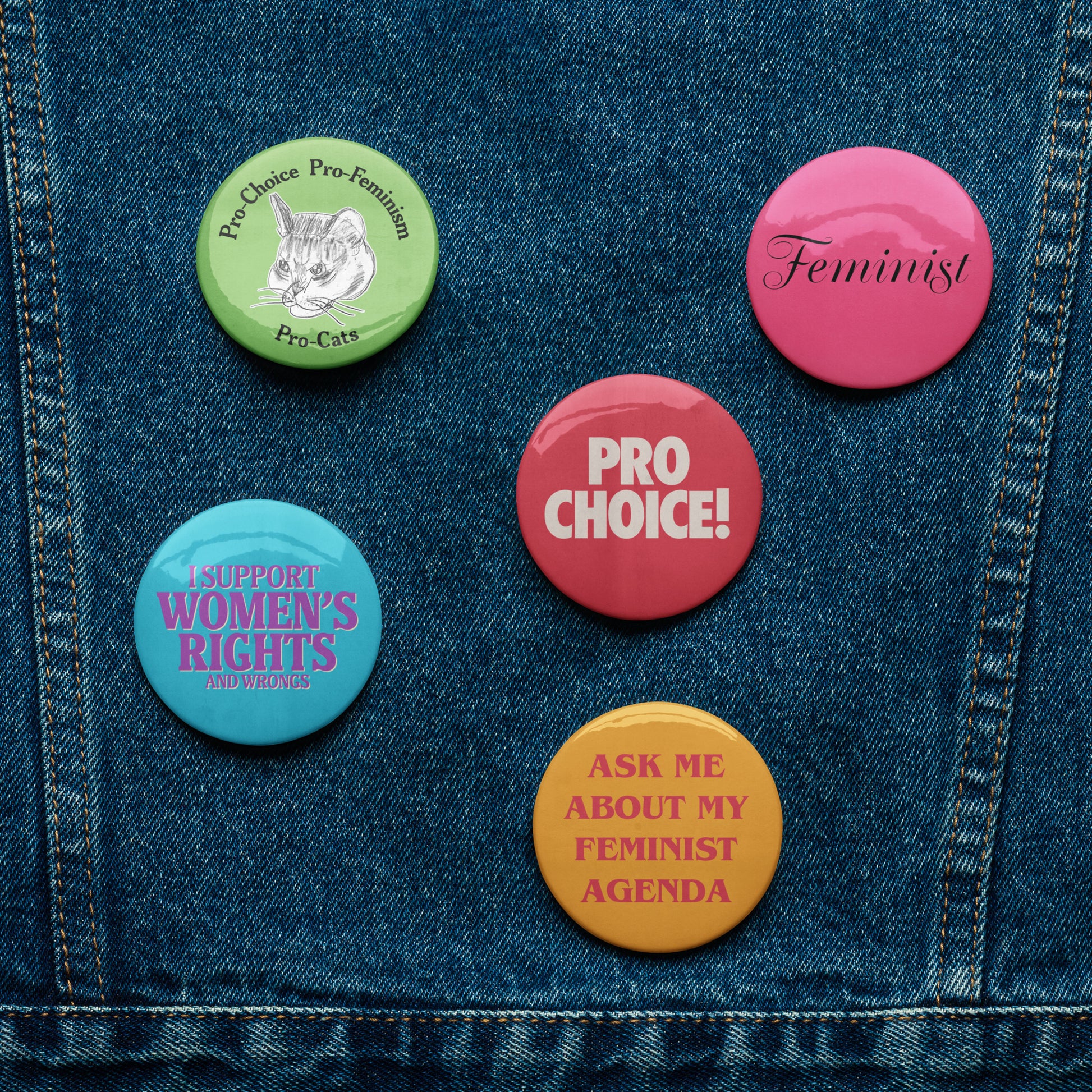 Set of five vintage-inspired feminist pin buttons on denim jacket featuring “Pro Choice,” “Feminist,” and “Ask Me About My Feminist Agenda” slogans.
