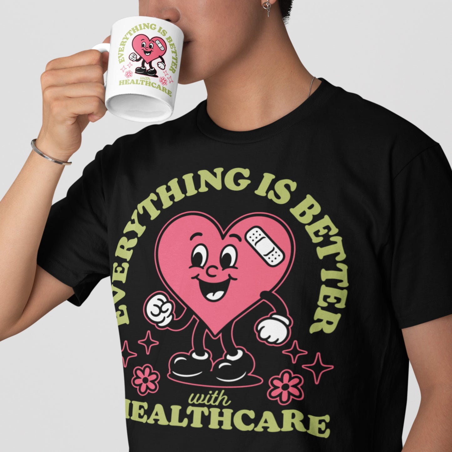 Person wearing the “Everything Is Better with Healthcare” t-shirt while holding a matching mug. Pink heart design stands out against the black tee.