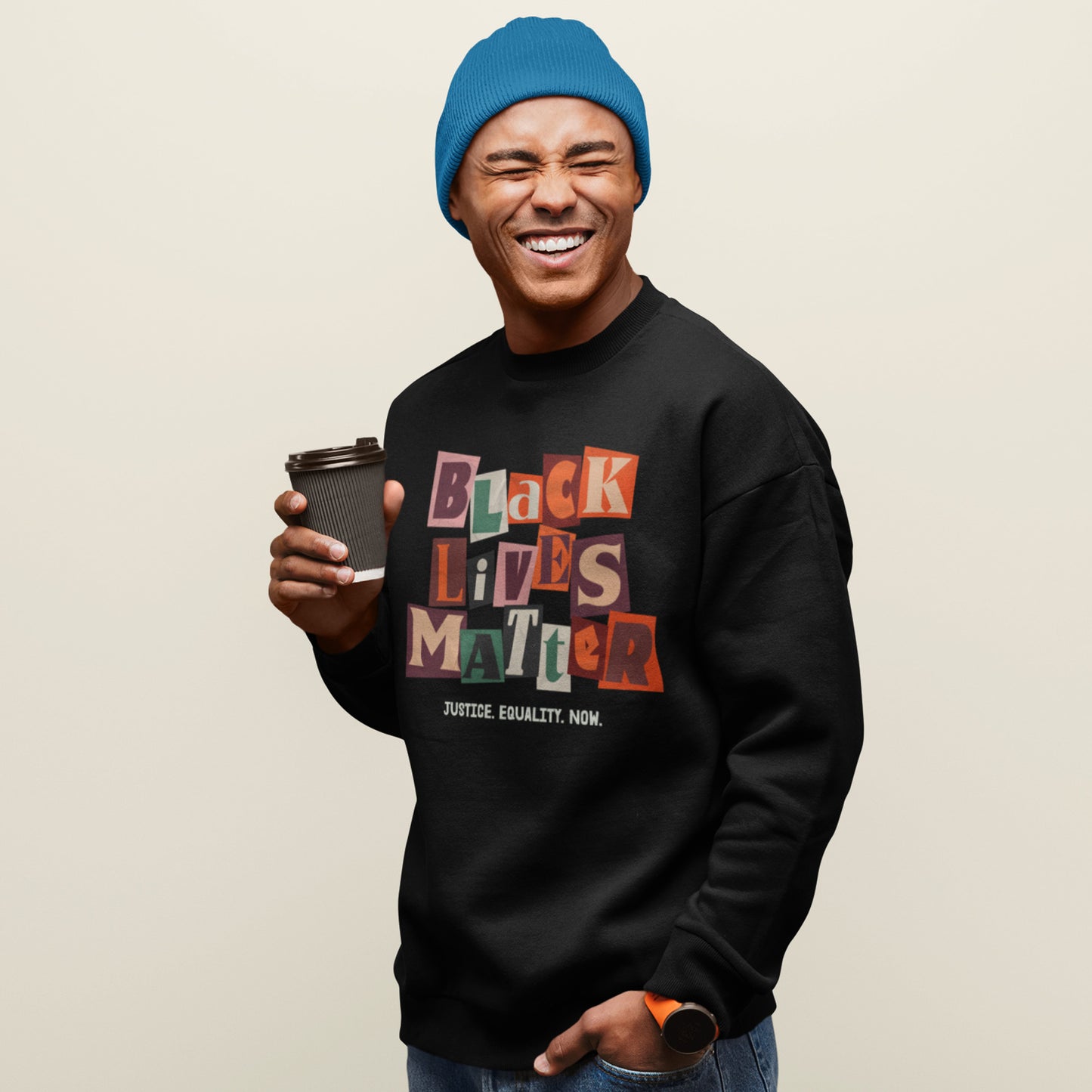 Person wearing a black premium sweatshirt featuring the colorful collage “BLACK LIVES MATTER” text and “JUSTICE. EQUALITY. NOW.” slogan, styled for racial-justice activism from Blue Wave USA.