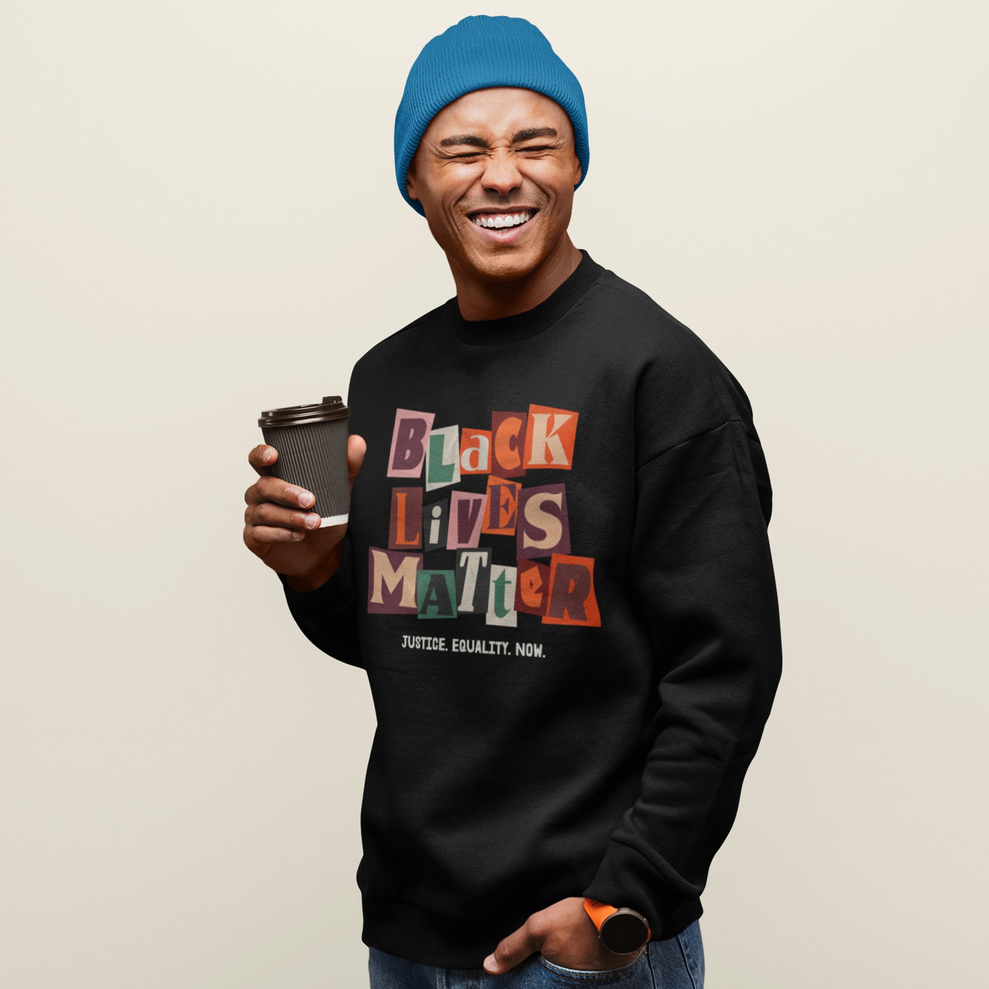 Person wearing a black premium sweatshirt featuring the colorful collage “BLACK LIVES MATTER” text and “JUSTICE. EQUALITY. NOW.” slogan, styled for racial-justice activism from Blue Wave USA.