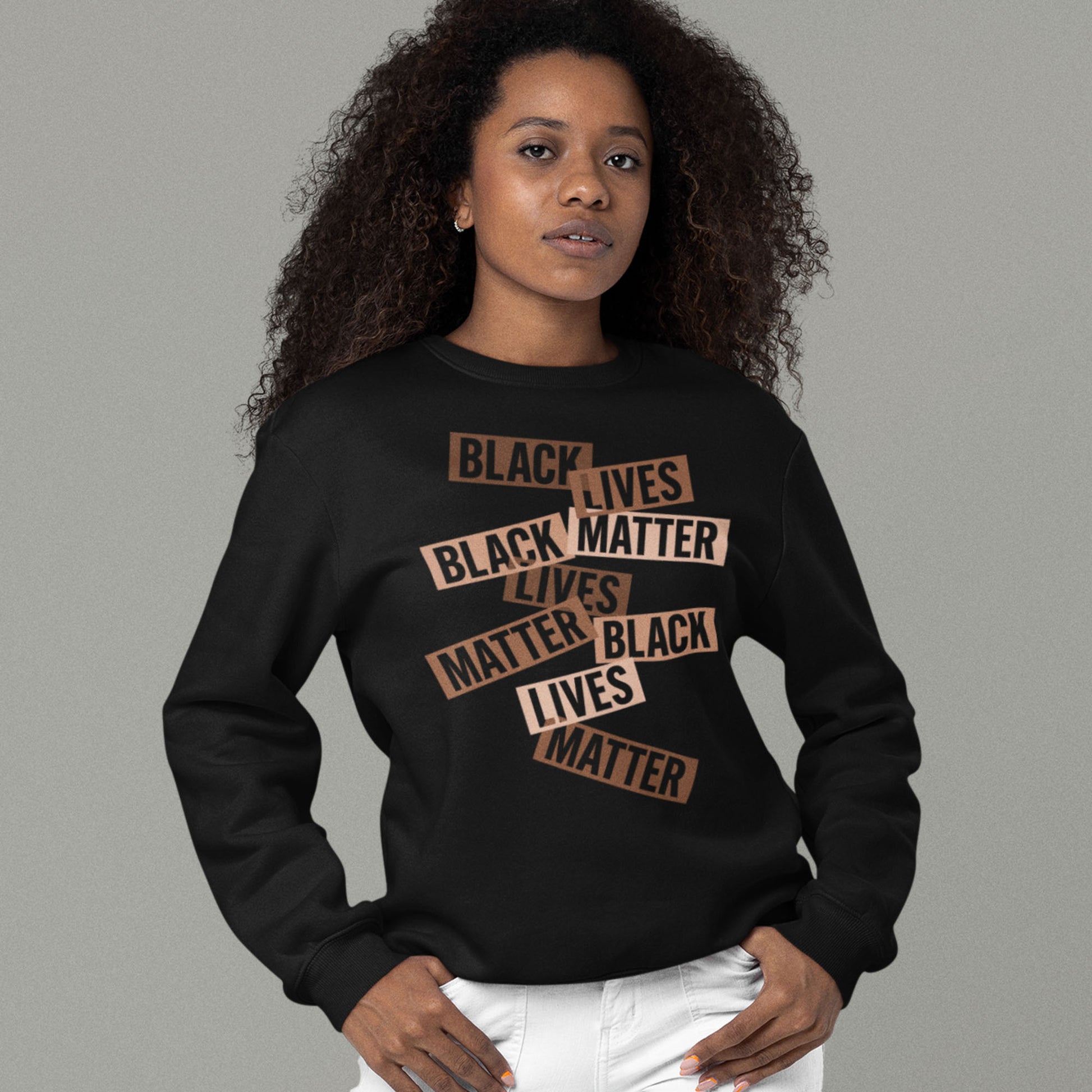 A model wearing a black sweatshirt printed with layered brown word strips forming the phrase “BLACK LIVES MATTER.” A collage-style activist design from Blue Wave USA.
