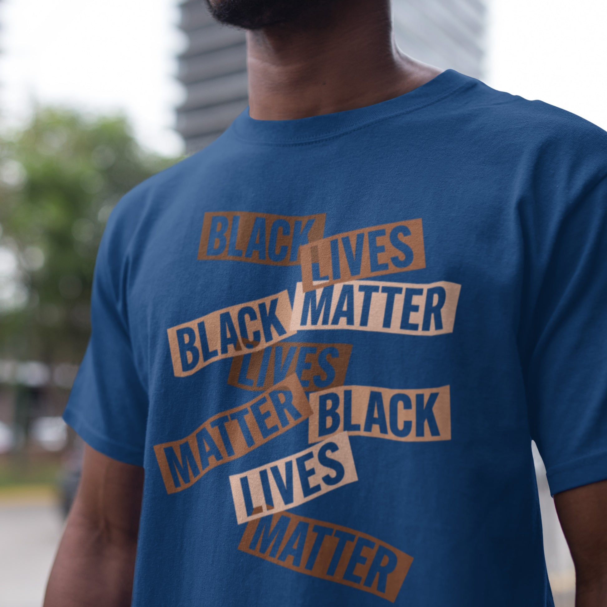 Person wearing a royal blue Black Lives Matter stacked text tee, standing outdoors. The bold layout and earthy lettering contrast beautifully against the bright fabric.