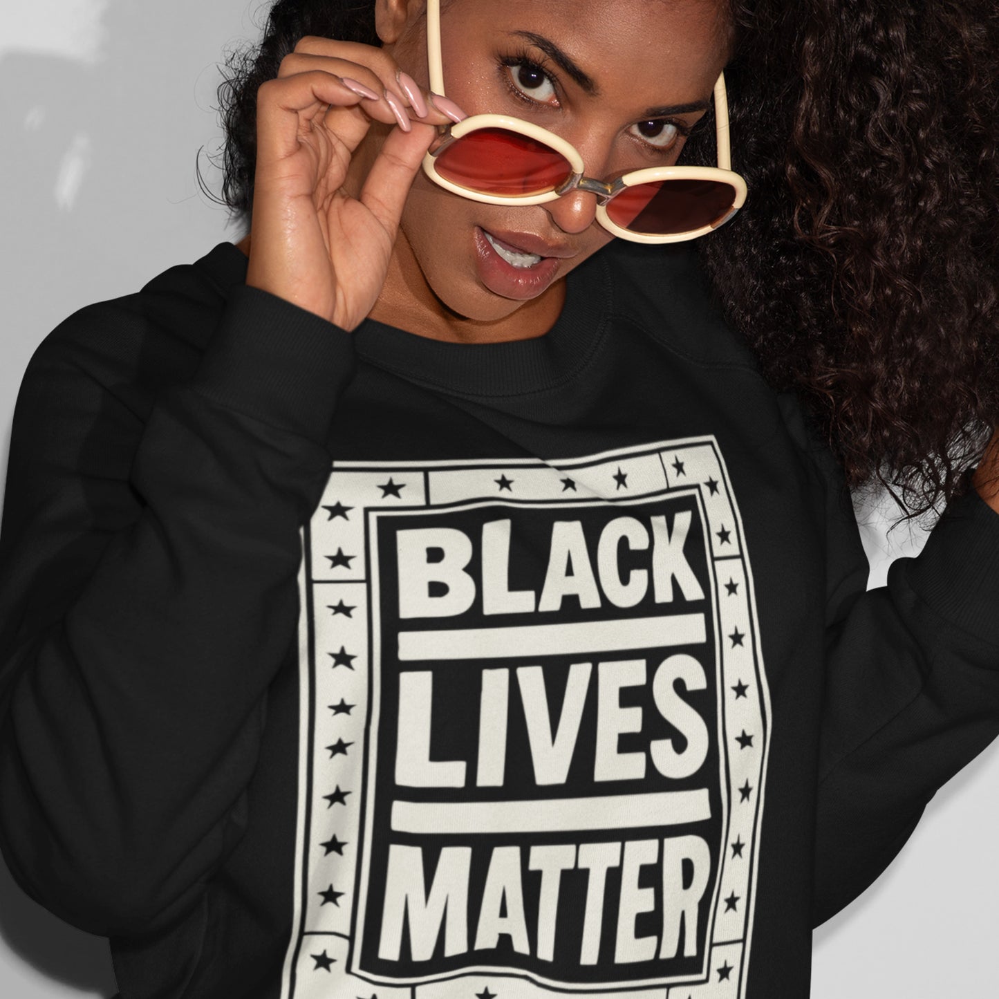 Model wearing a black unisex sweatshirt with the cream framed “BLACK LIVES MATTER” print, styled casually and highlighting a clean racial-justice design from Blue Wave USA.