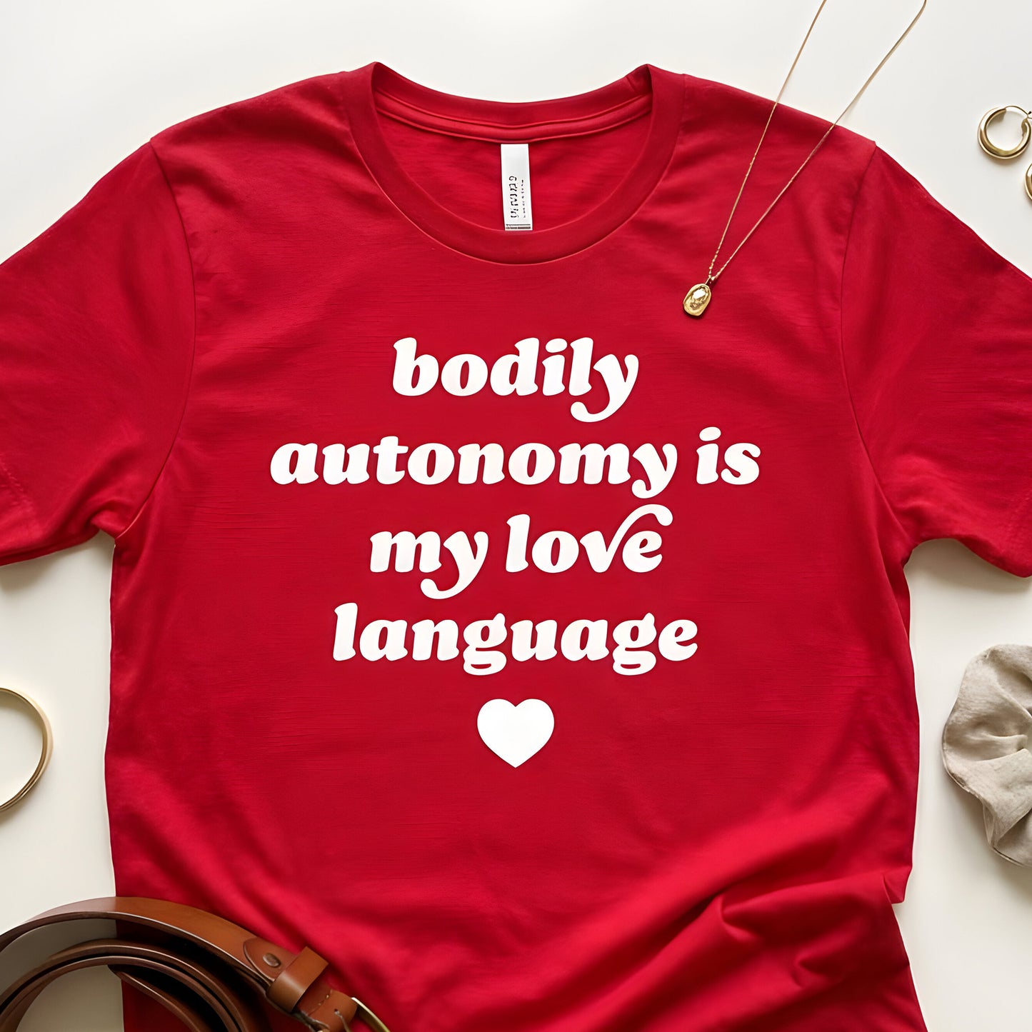 Unisex t-shirt flat-lay with jewelry accents showcasing retro text and heart graphic reading “bodily autonomy is my love language,” a justice-focused Valentine’s Day design from Blue Wave USA.