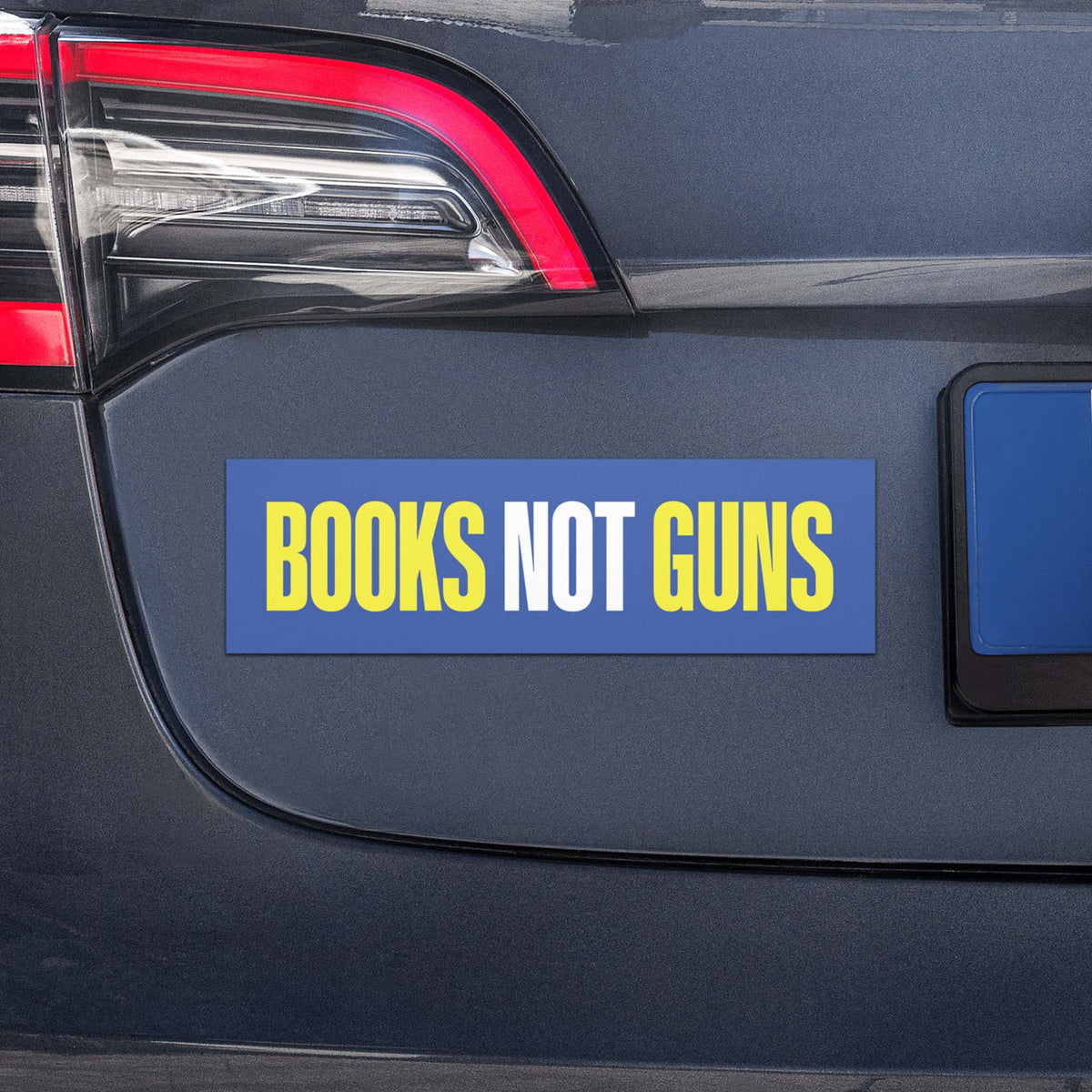 Blue “Books Not Guns” car magnet displayed on the rear of a vehicle, showing the bold yellow and white design in everyday use.