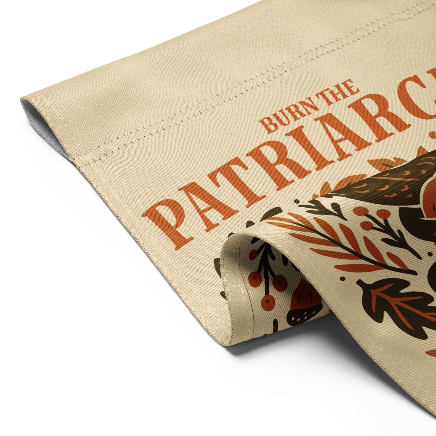 Close-up of rolled beige fabric showing the dragon’s tail and pumpkin detail from the “Burn the Patriarchy” feminist garden flag design.