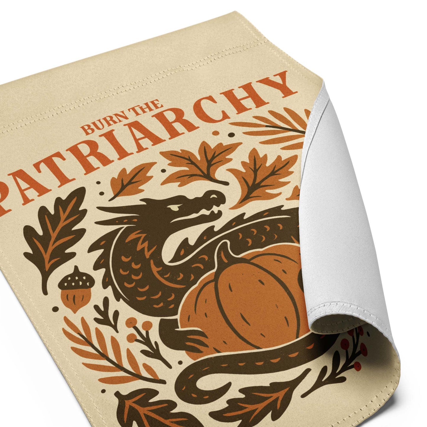 Folded corner close-up of “Burn the Patriarchy” dragon and botanical design printed on linen-textured garden flag fabric.