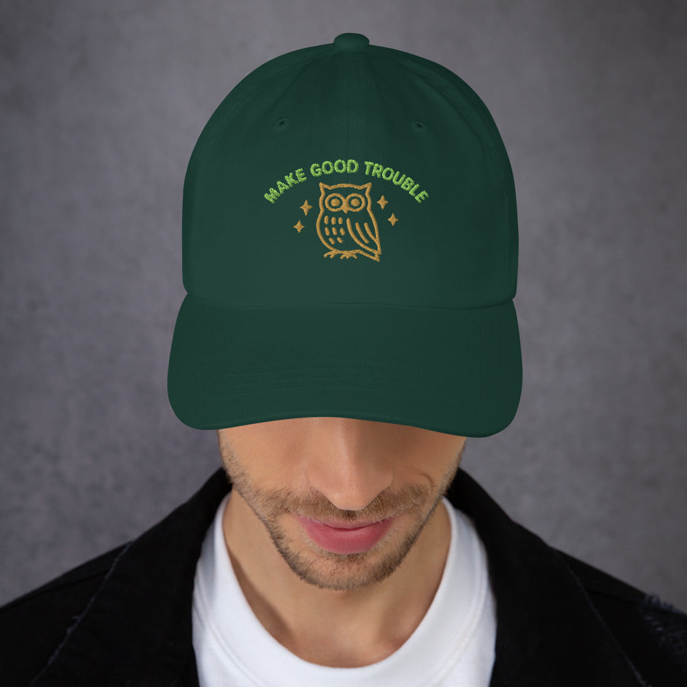 Person wearing a forest green embroidered dad hat with the golden owl and “MAKE GOOD TROUBLE” text, a soft-structured civil rights design from Blue Wave USA.
