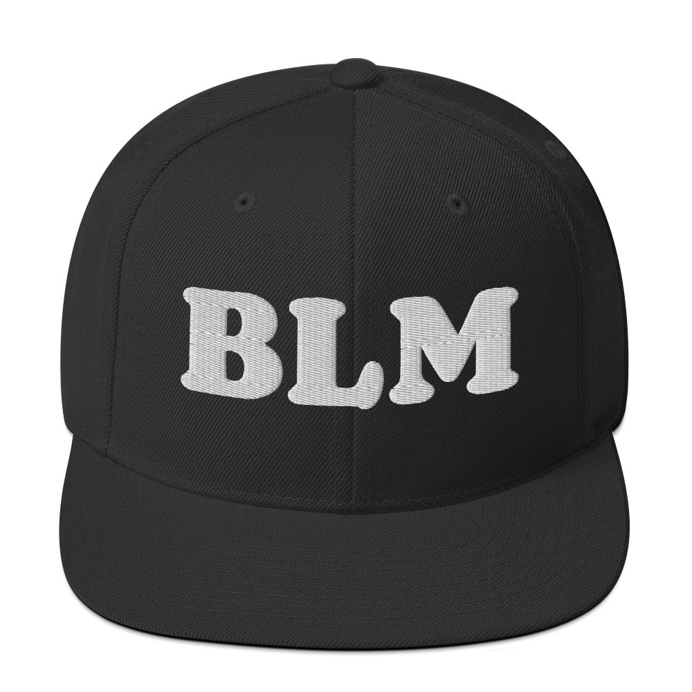 Black snapback hat with raised embroidered lettering reading “BLM,” bold minimalist design in tonal black thread on structured crown, flat brim style.