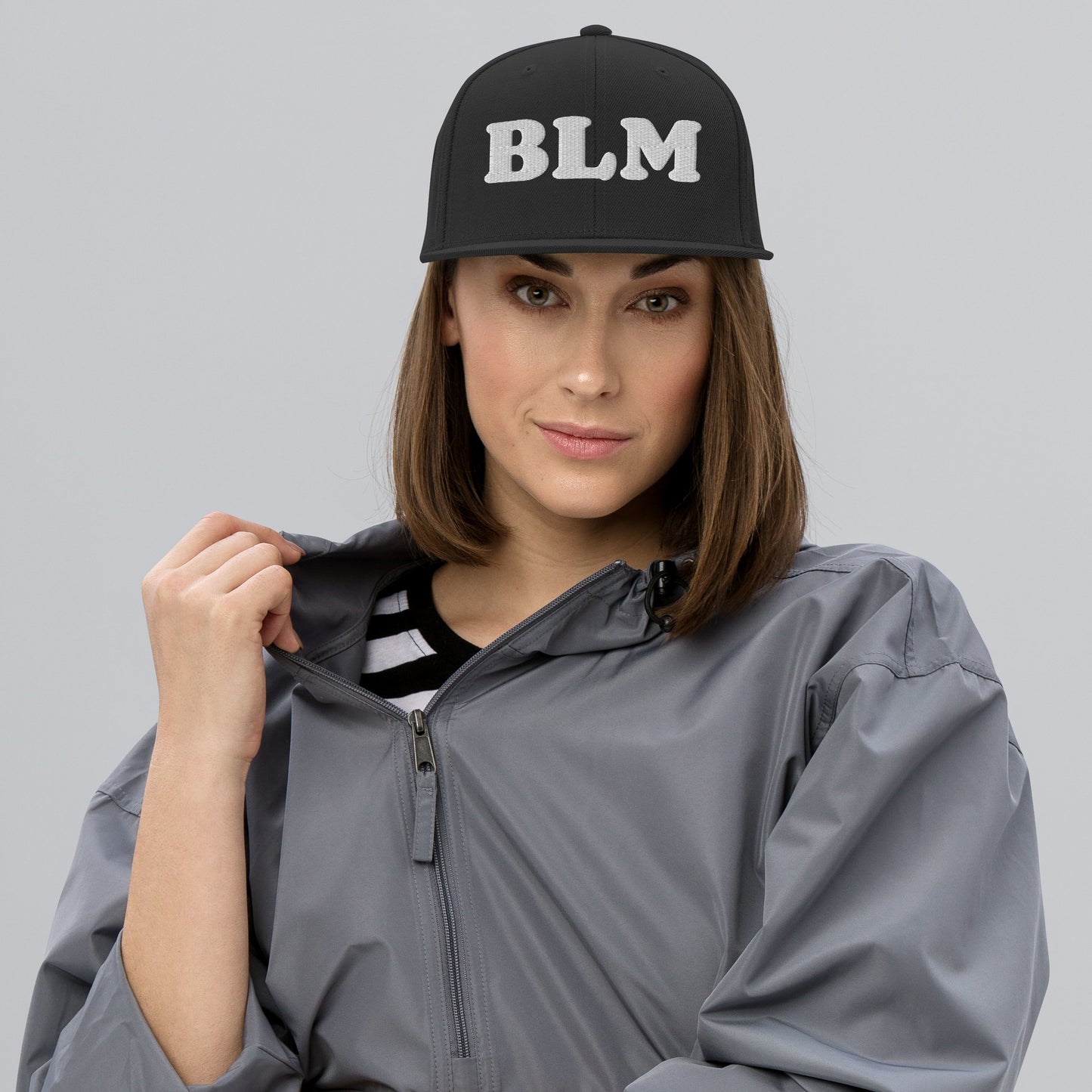 Model wearing a black snapback hat with raised embroidered “BLM” lettering on the front, minimalist activist headwear from Blue Wave USA.