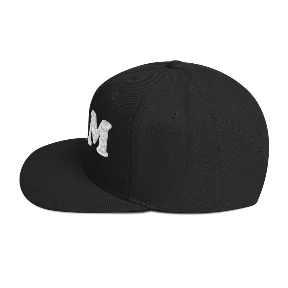 Side angle of a black snapback hat with flat brim and raised “BLM” embroidery, showing structured crown and clean modern silhouette.
