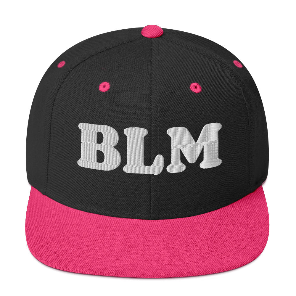 Black snapback hat with pink brim and tonal embroidered “BLM” lettering, playful activist design with flat brim and structured crown.