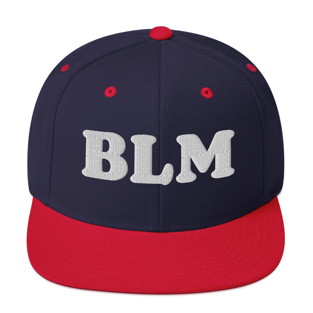 Navy snapback hat with red brim featuring raised embroidered “BLM” text, classic two-tone activist headwear with flat brim design.