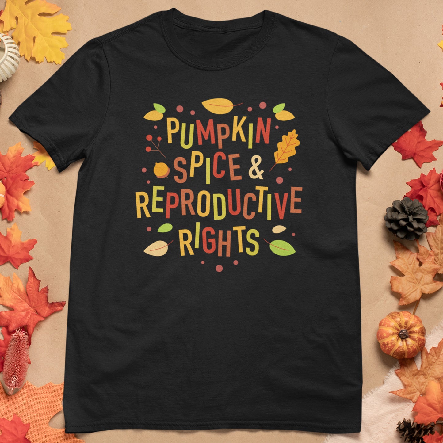 Black Black Pumpkin Spice and Reproductive Rights t-shirt with colorful text 'Pumpkin Spice & Reproductive Rights' on a beige background with autumn leaves and pumpkins.