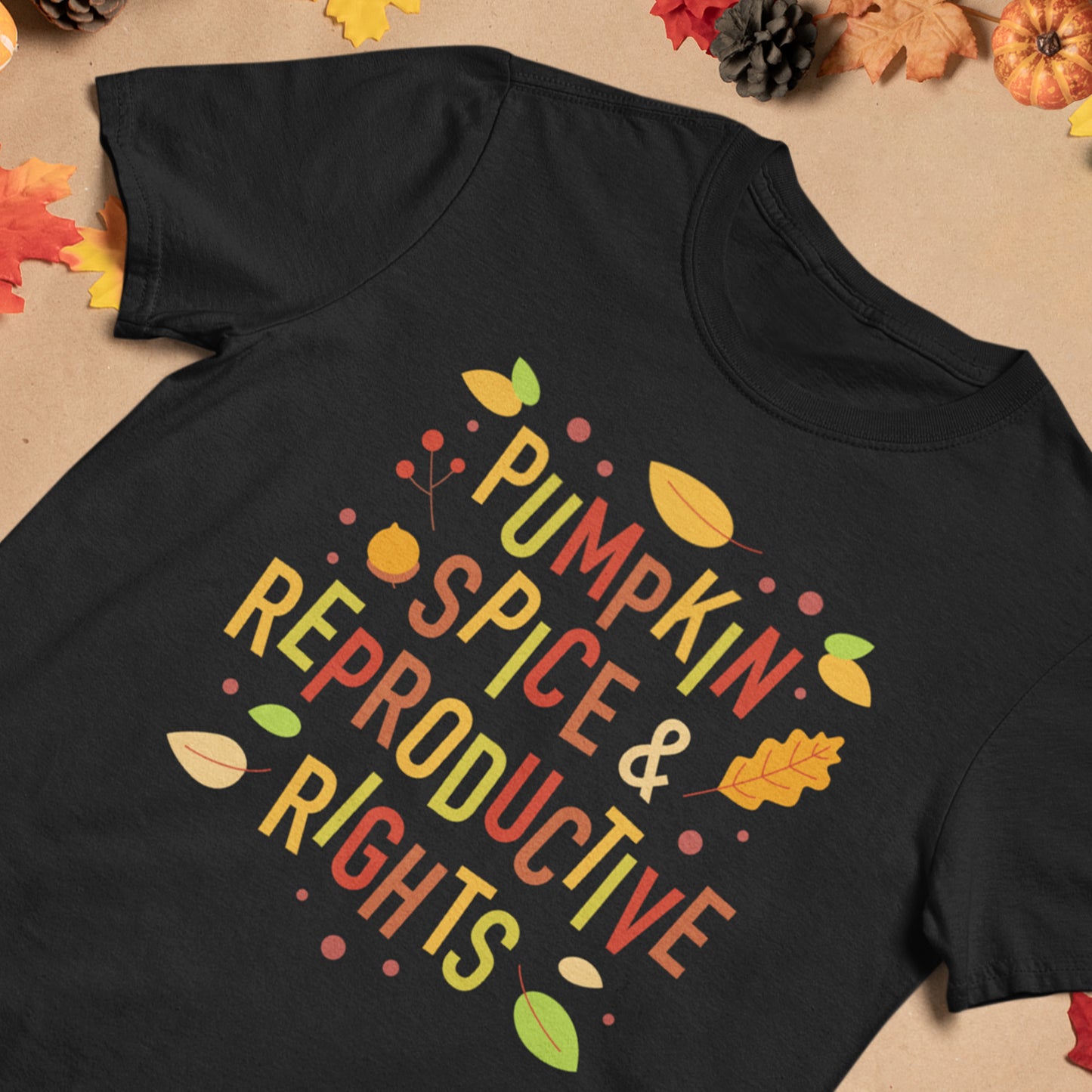 Black Black Pumpkin Spice and Reproductive Rights t-shirt with colorful text 'Pumpkin Spice & Reproductive Rights' on a beige background with autumn leaves and pumpkins.