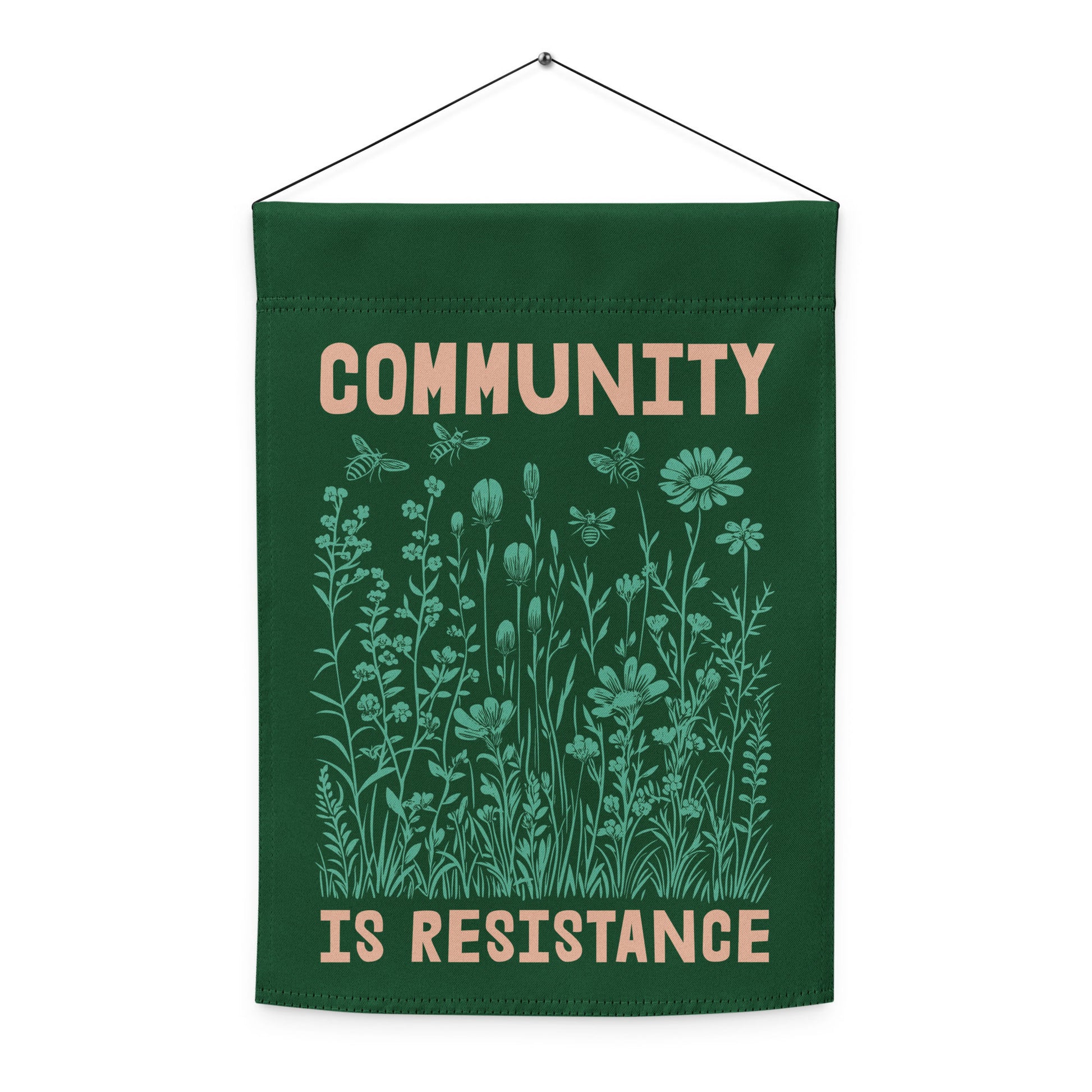 The Community Is Resistance garden flag displayed vertically indoors, doubling as activist art. Mint floral design and soft typography create a calm yet defiant aesthetic.
